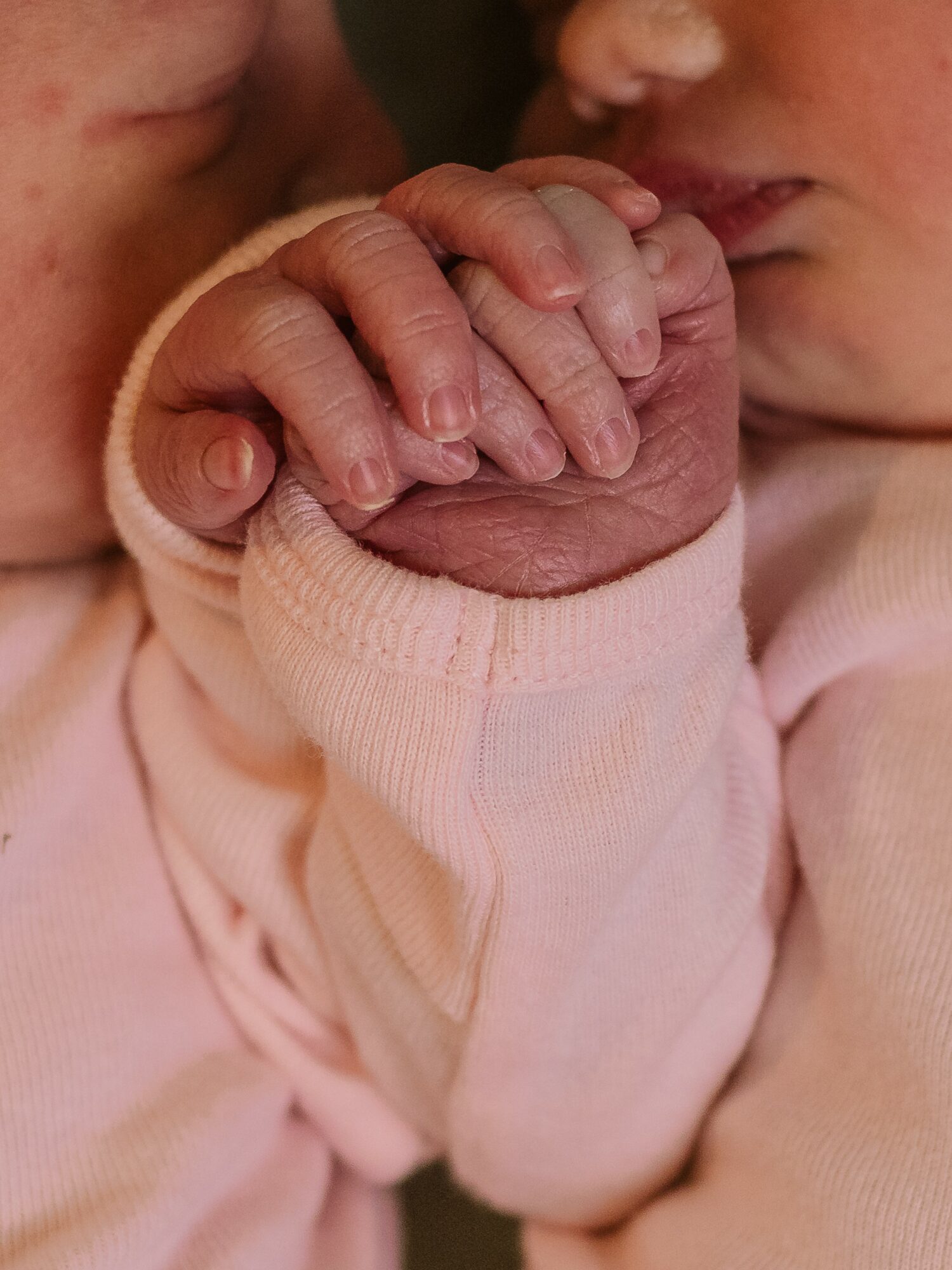 Close-up of two children holding hands, one with a pink sleeve, showing fingers intertwined.