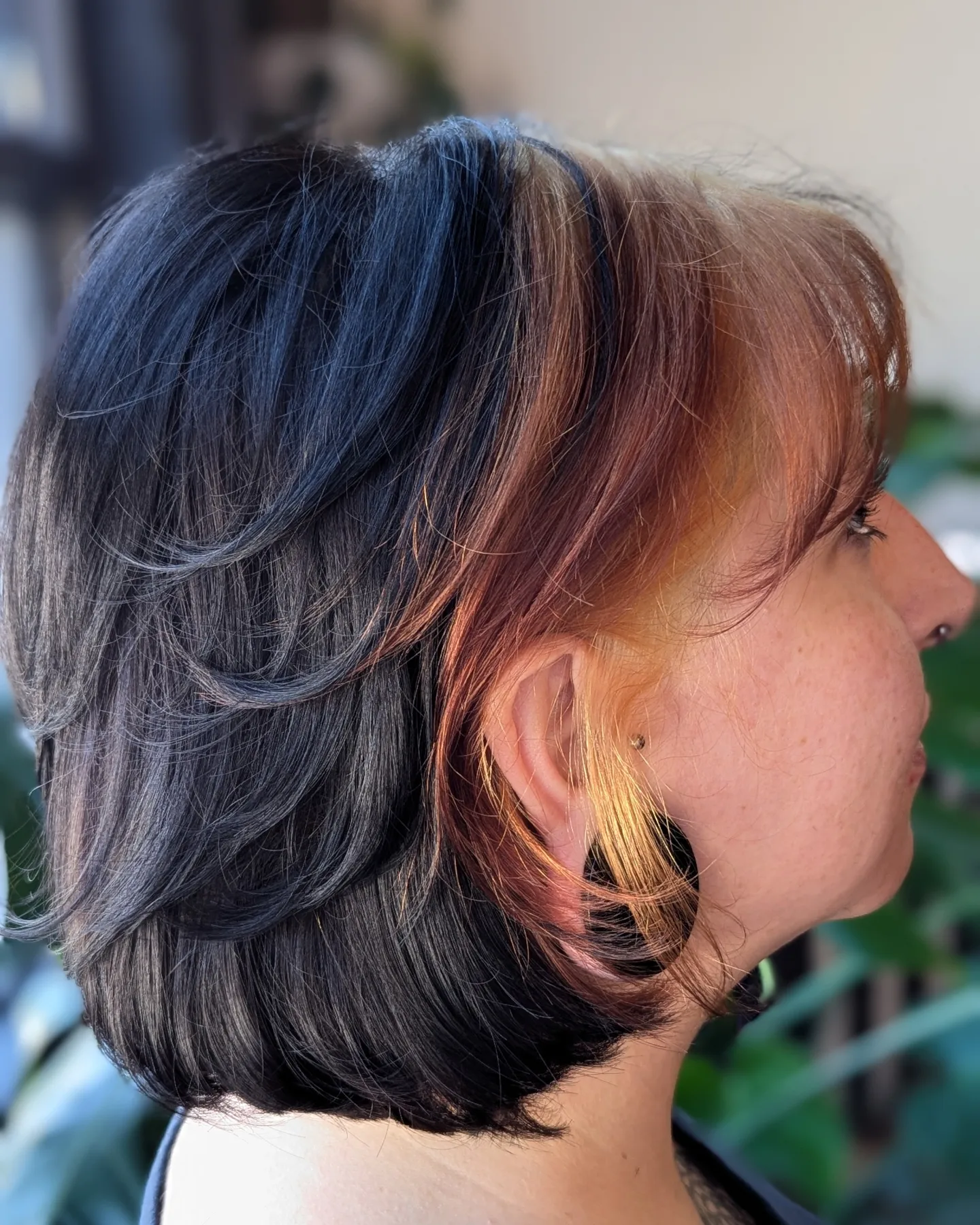 Side profile of a woman with short, layered hair with black, brown, and blonde highlights, and a gold earring.