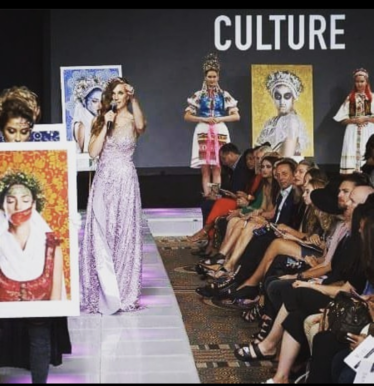 Fashion show with models on stage and audience watching, large artwork displayed, and the word 'CULTURE' on screen.