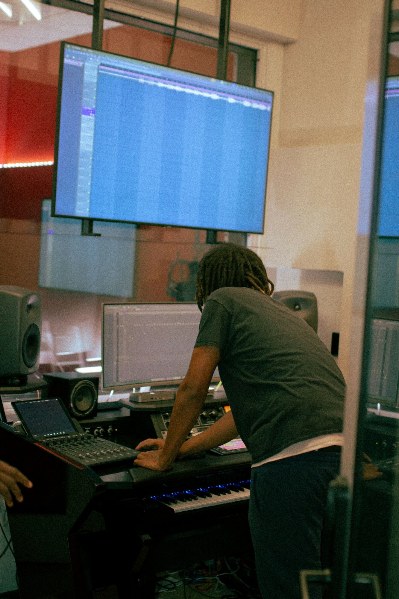 Person working at a music production station with multiple monitors and audio equipment in a room.