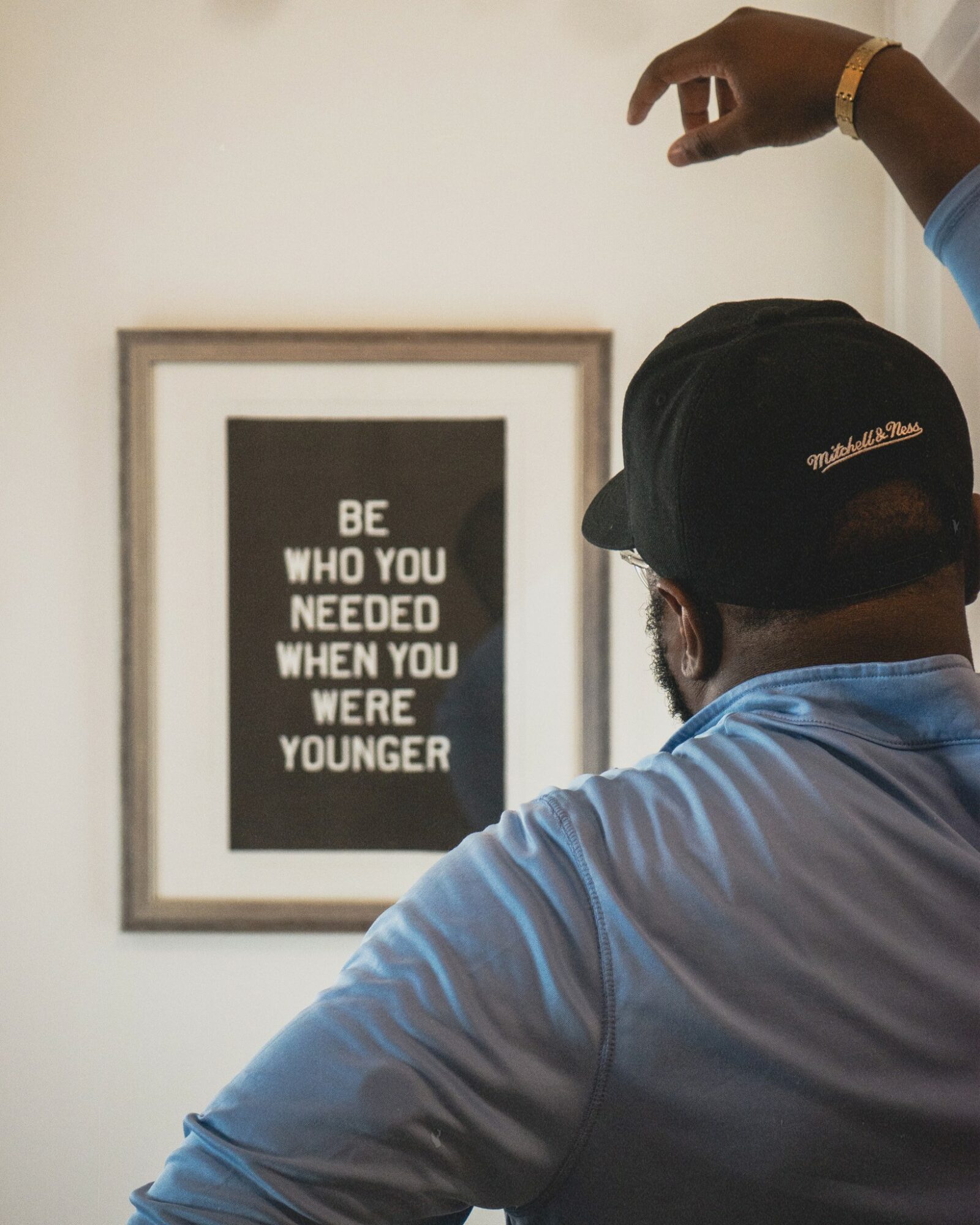 Person wearing a black cap and blue shirt looking at a framed quote on the wall.