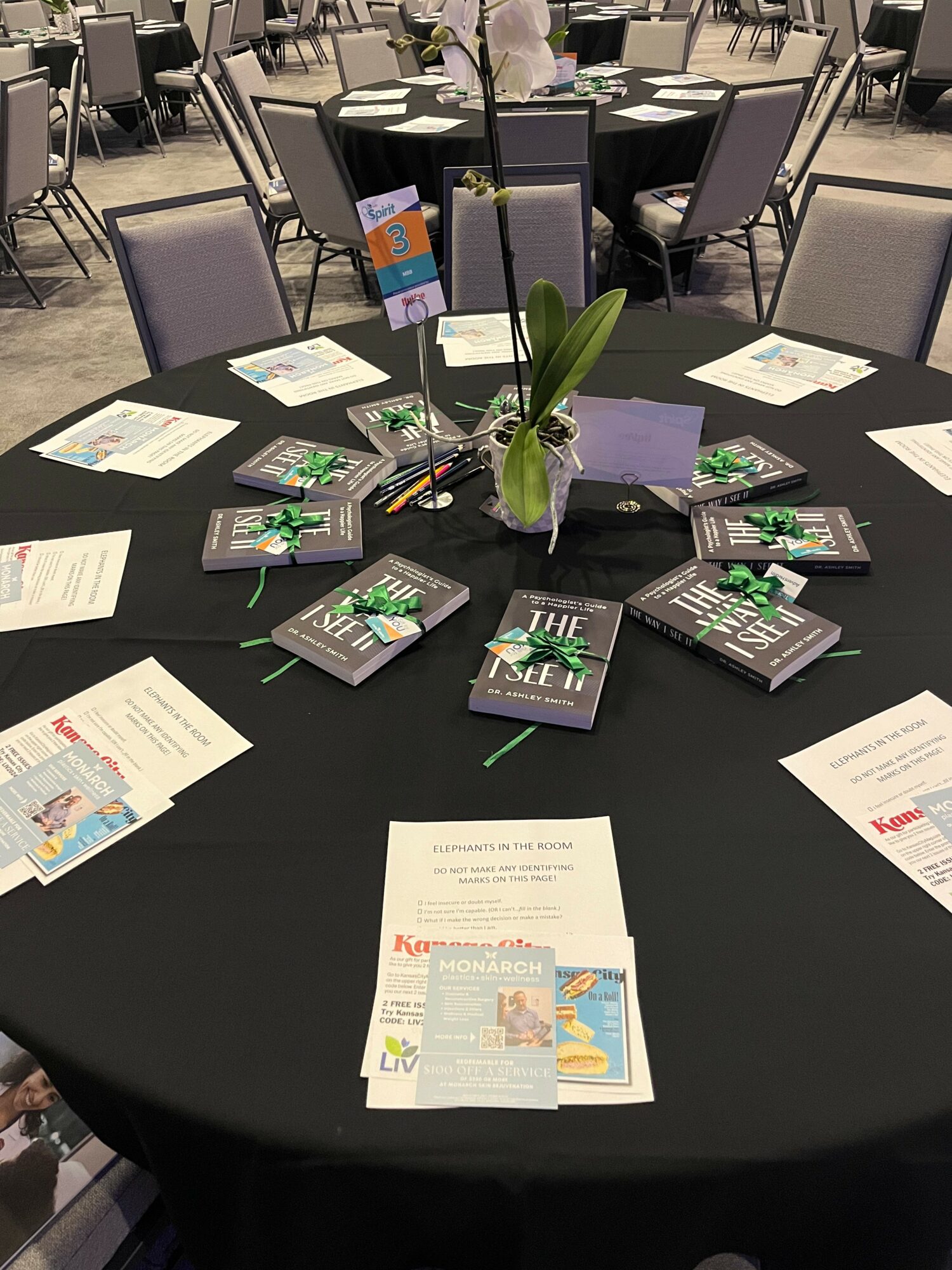 Round table with books, papers, and a small plant in a conference room, surrounded by chairs.