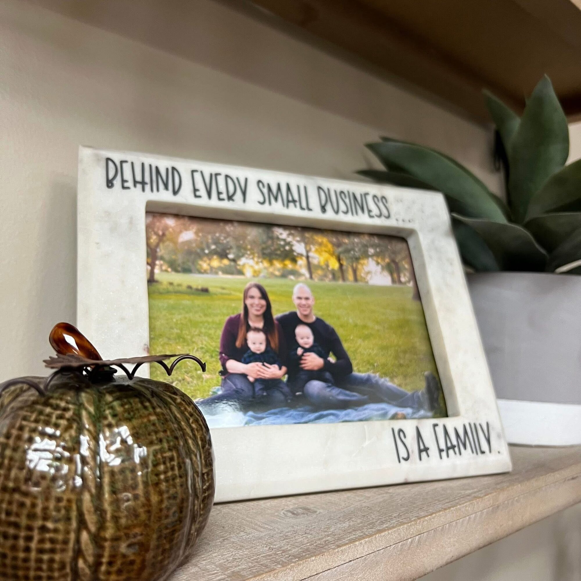 Framed photo of two people sitting outdoors on grass, with a plant and decorative object nearby, on a wooden surface.
