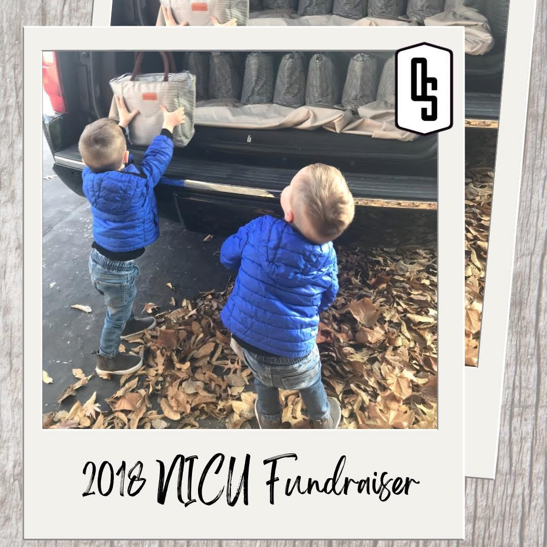 Two children in blue jackets pick up leaves near a vehicle with shoes on display inside, outdoors with fallen leaves.