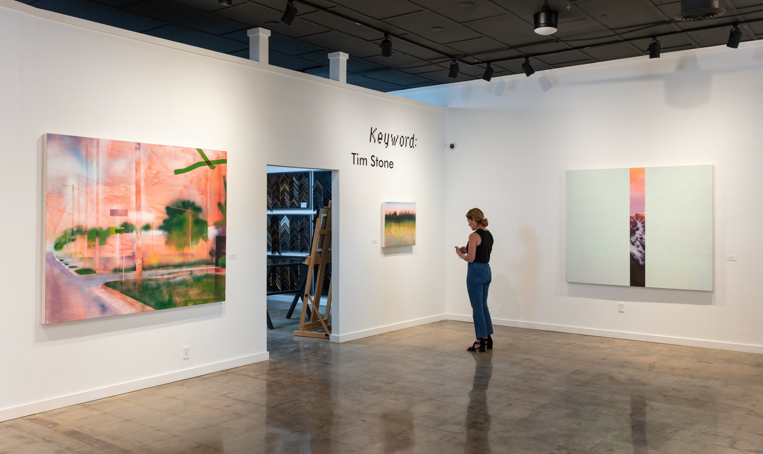Person viewing artwork in gallery with paintings on white walls and polished floor.