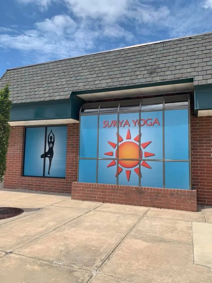 Building with large window displaying a yoga poster with a sun and a person in a yoga pose, blue sky above.