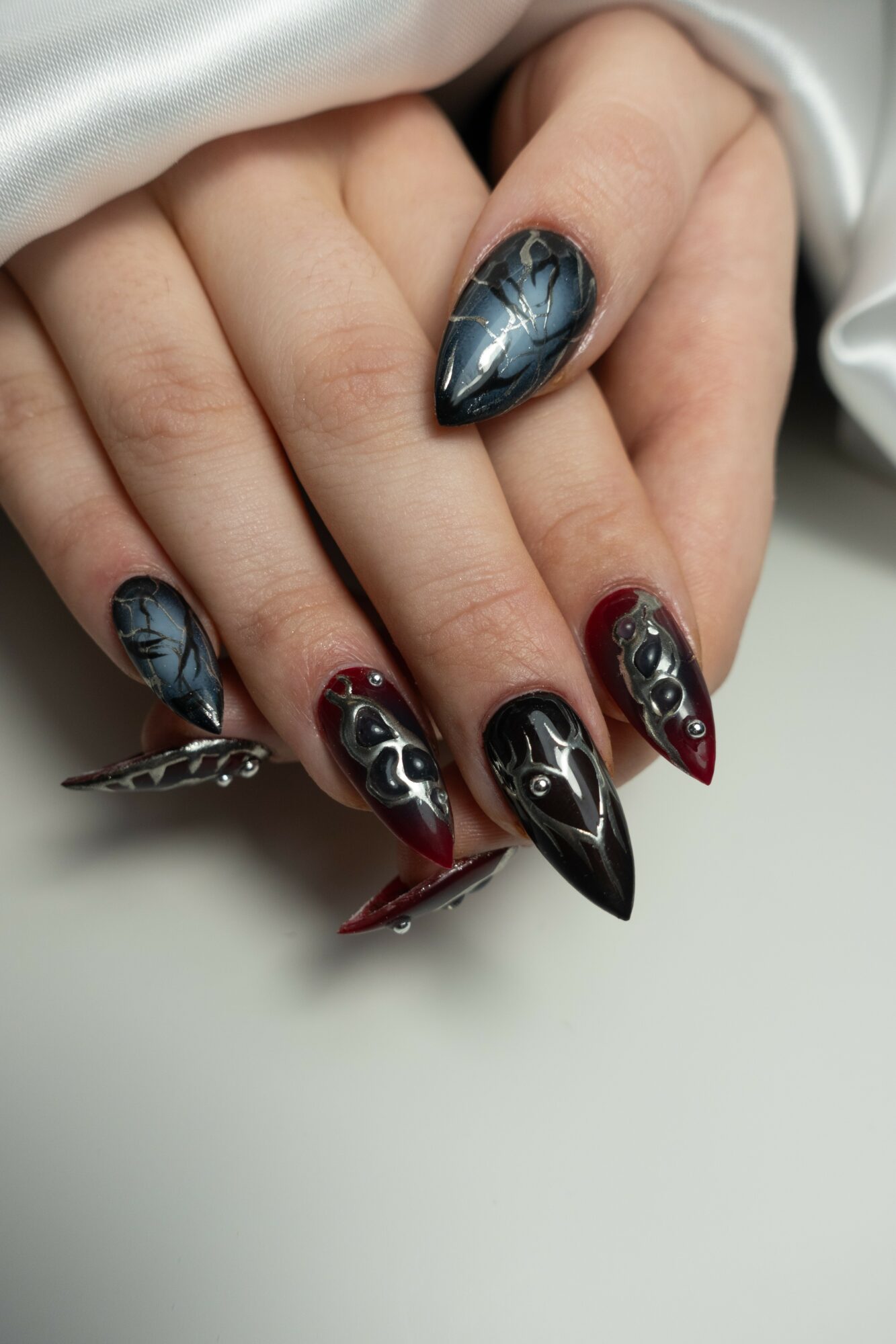 Close-up of hand with black and red nail art, featuring metallic and flame designs, on a white background.