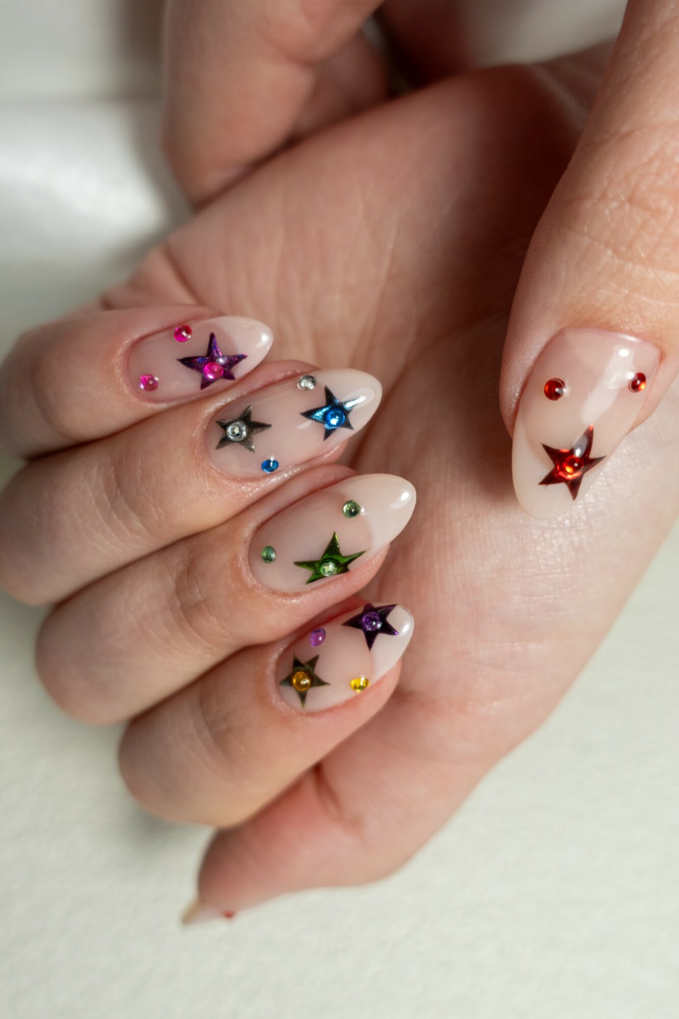 Close-up of a hand with decorated nails featuring colorful star and dot designs, with a light background.