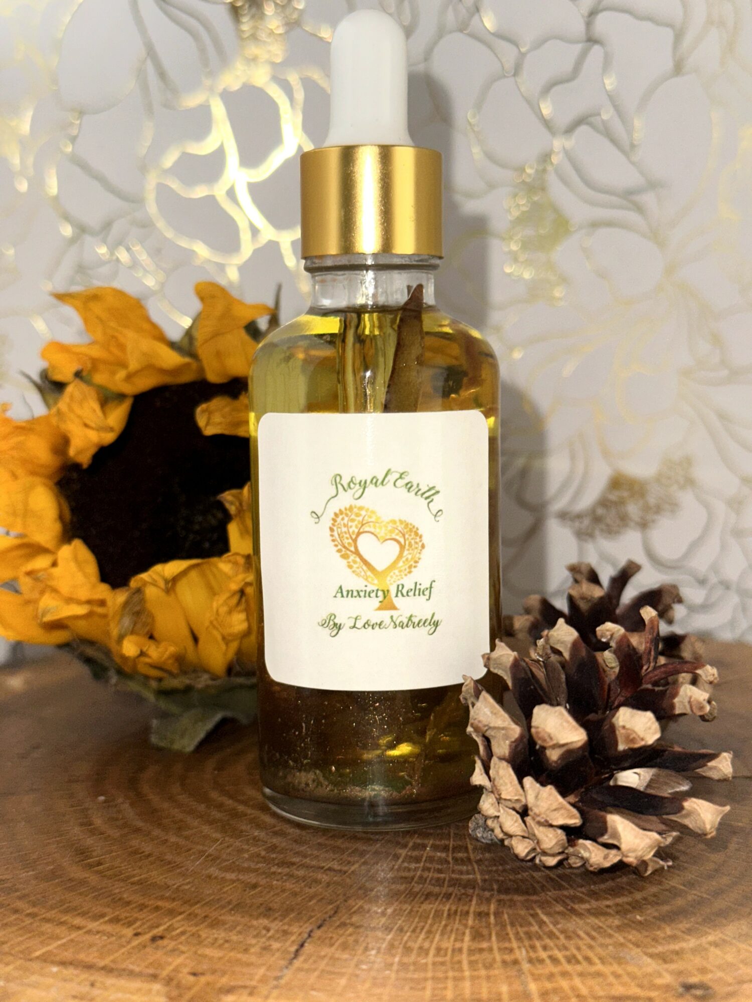 Dropper bottle with a white label featuring a heart and text, surrounded by dried flowers and pinecone, on a wooden surface.