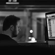 Person working on a computer in a dimly lit environment, focused on the screen, with blurred background.