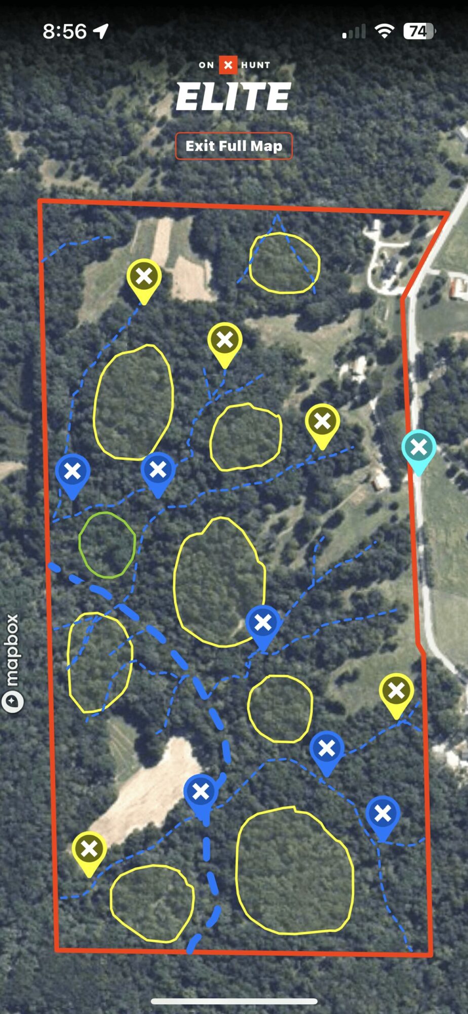 Aerial view of a wooded area with multiple marked zones and icons, including yellow circles and blue crosses, within a red boundary.