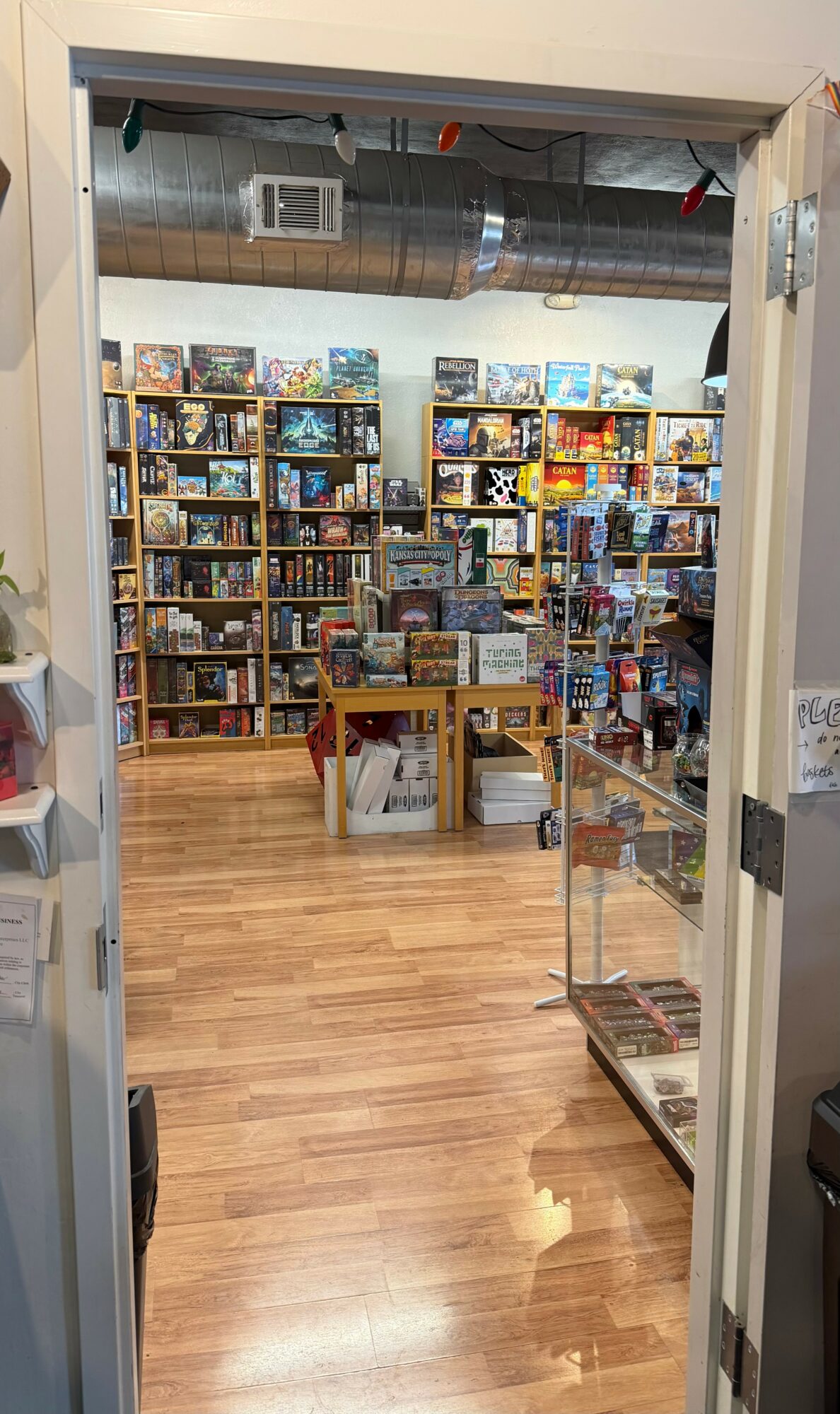 View through doorway into a store with wooden floors, shelves filled with books and games, and a table in the center.