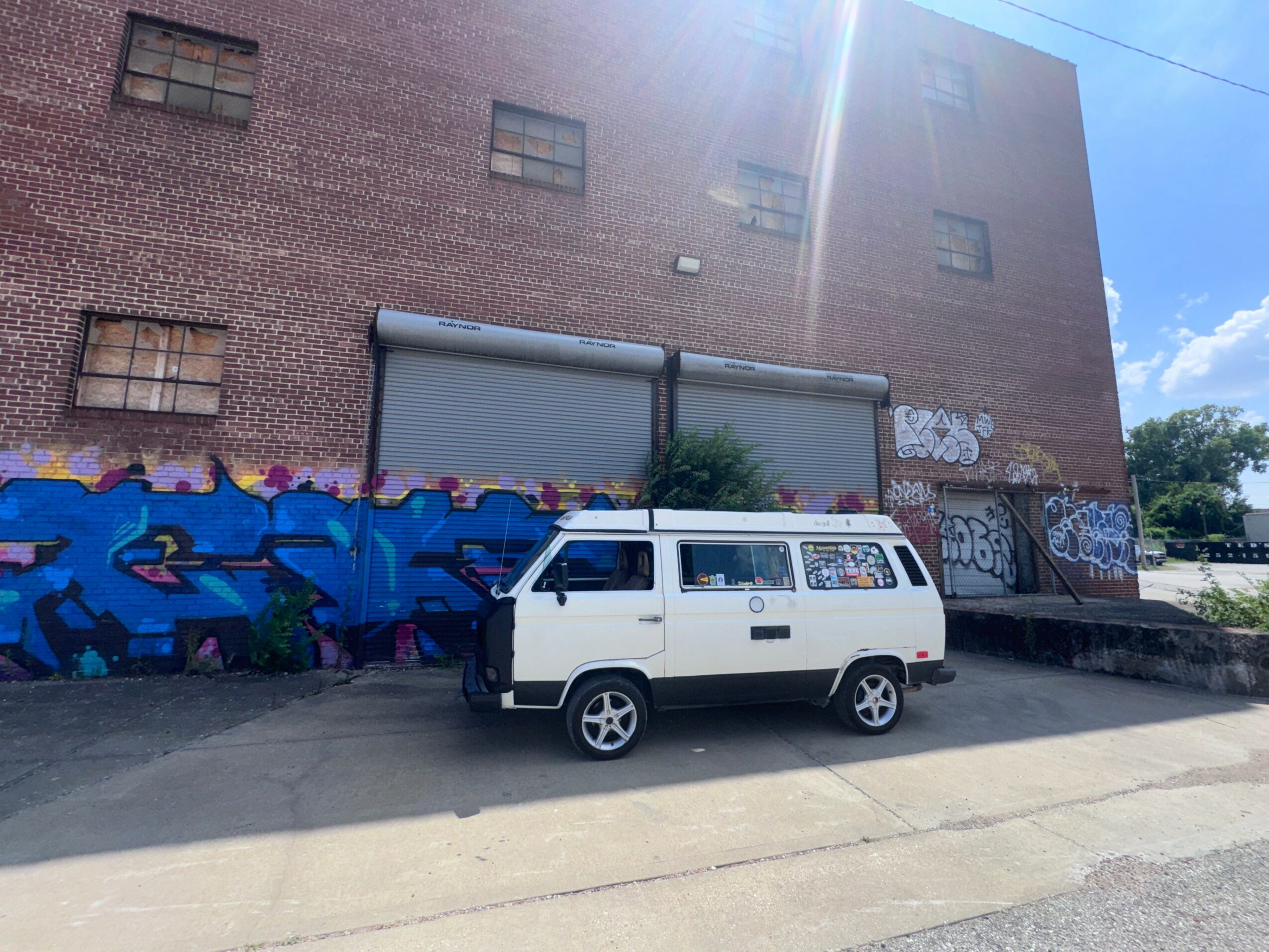White van parked in front of a brick building with graffiti, under a clear blue sky.