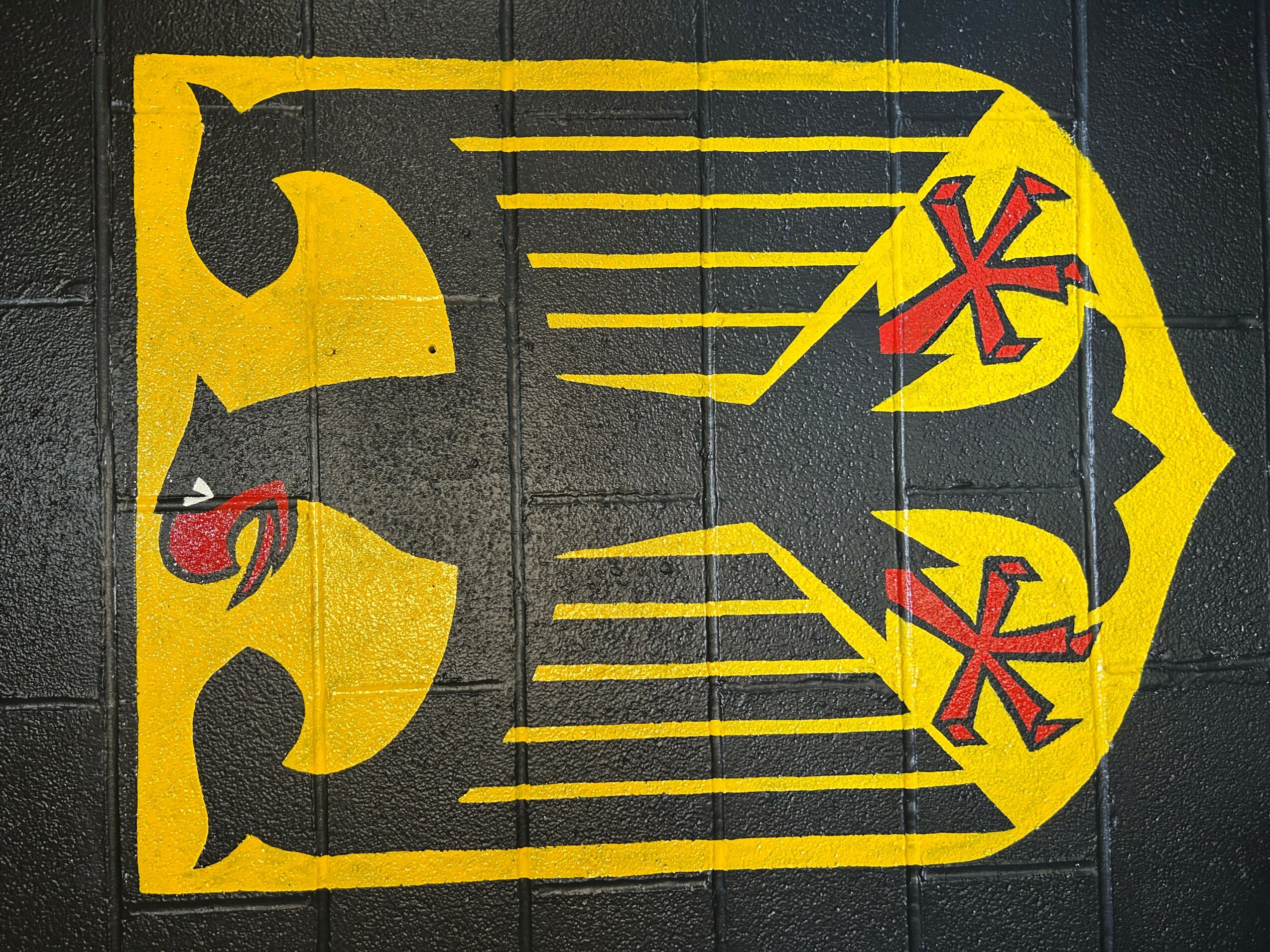 A stylized yellow and black eagle with red accents on a yellow background, facing right, with lines extending from its head.
