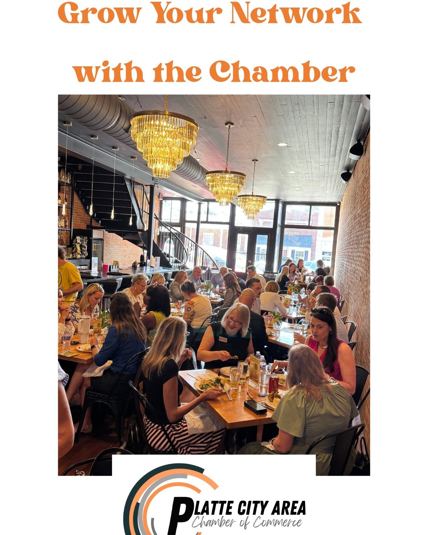 People dining in a restaurant with large windows, chandeliers, and a staircase, engaging in conversations and enjoying meals.