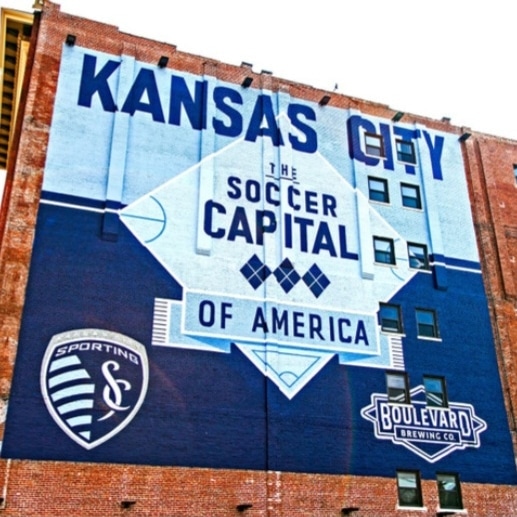 Mural on building promoting Kansas City soccer capital of America, with logos and text in blue and white.