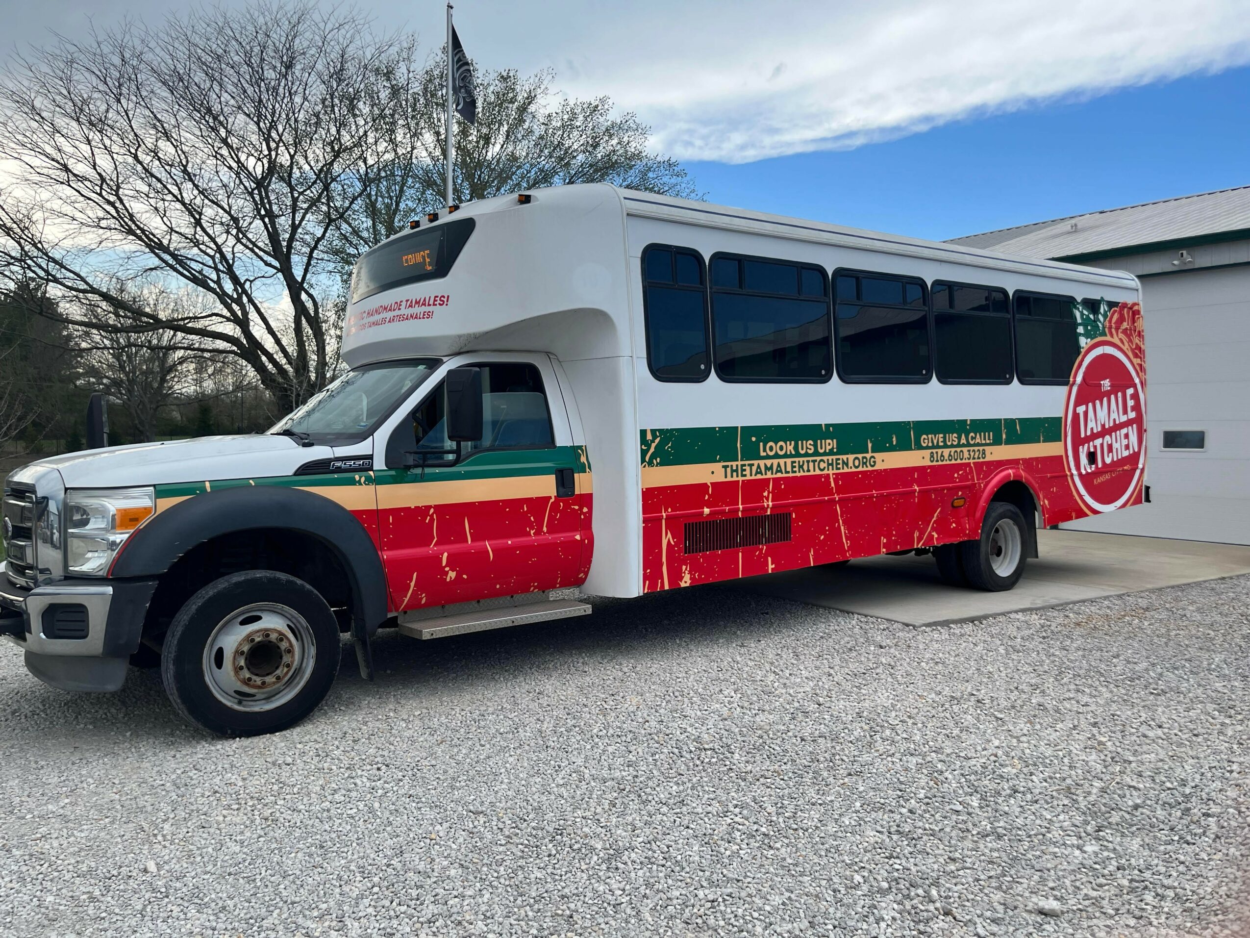 Bus decorated with Christmas theme, red and green colors, and a large red circle with white text, parked outdoors.