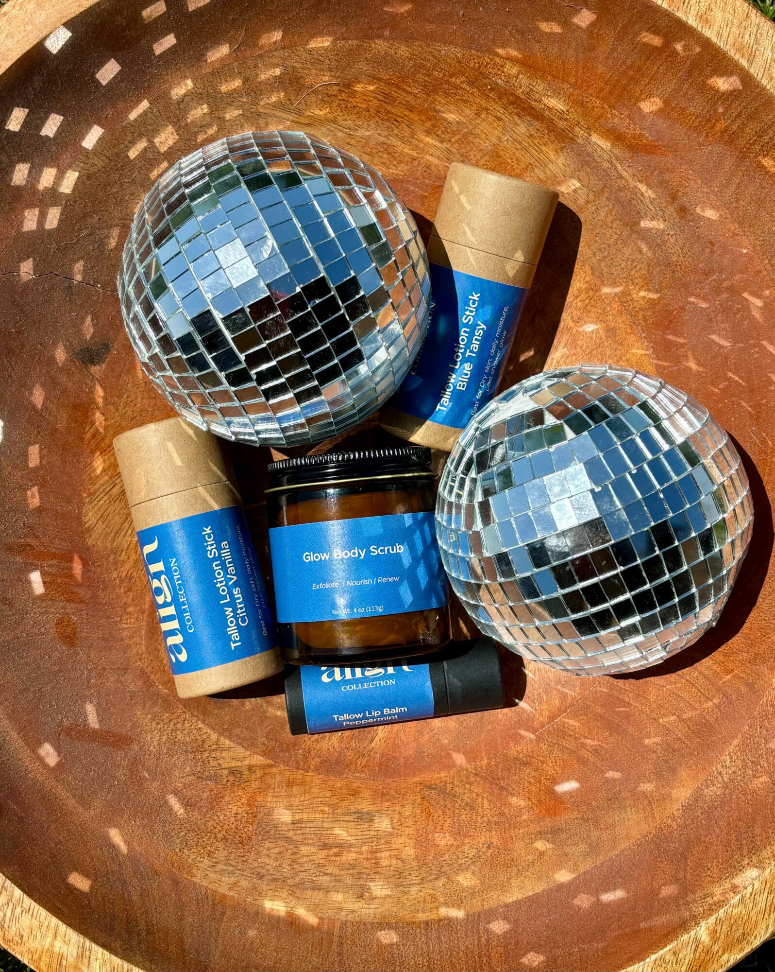 Two disco balls and several skincare products in a wooden bowl, with blue labels and beige caps.