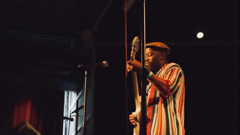 Person holding a microphone on stage with a dark background and a bright light in the distance.