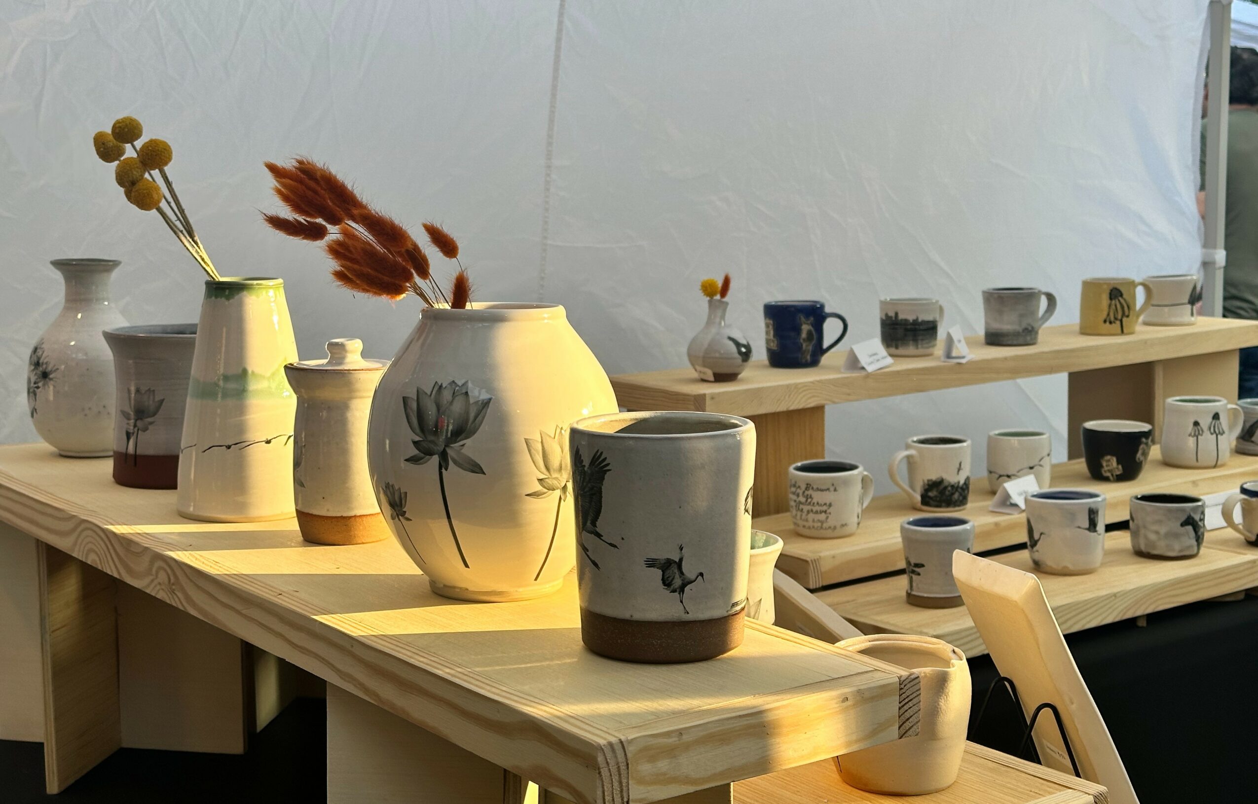 Display of various ceramic vases and cups on a wooden table with a white background.