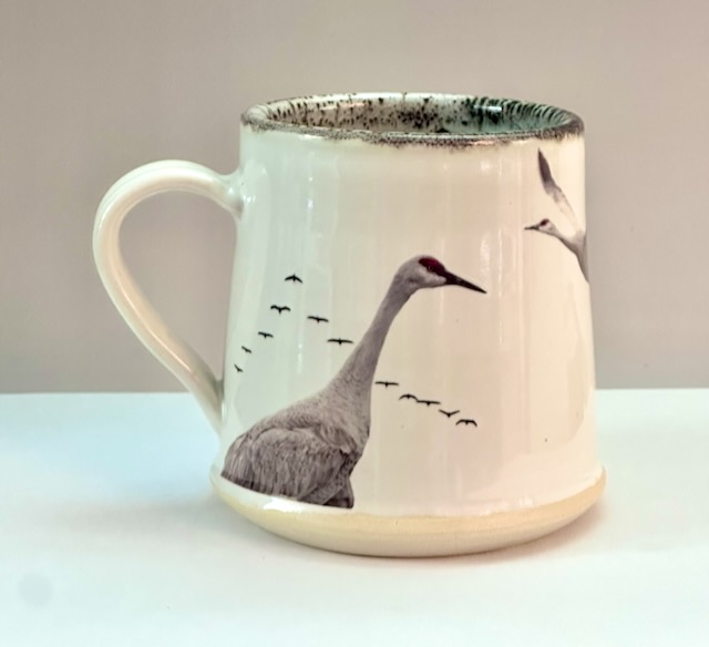 Ceramic mug with a crane and flying birds design, placed on a white surface against a plain background.