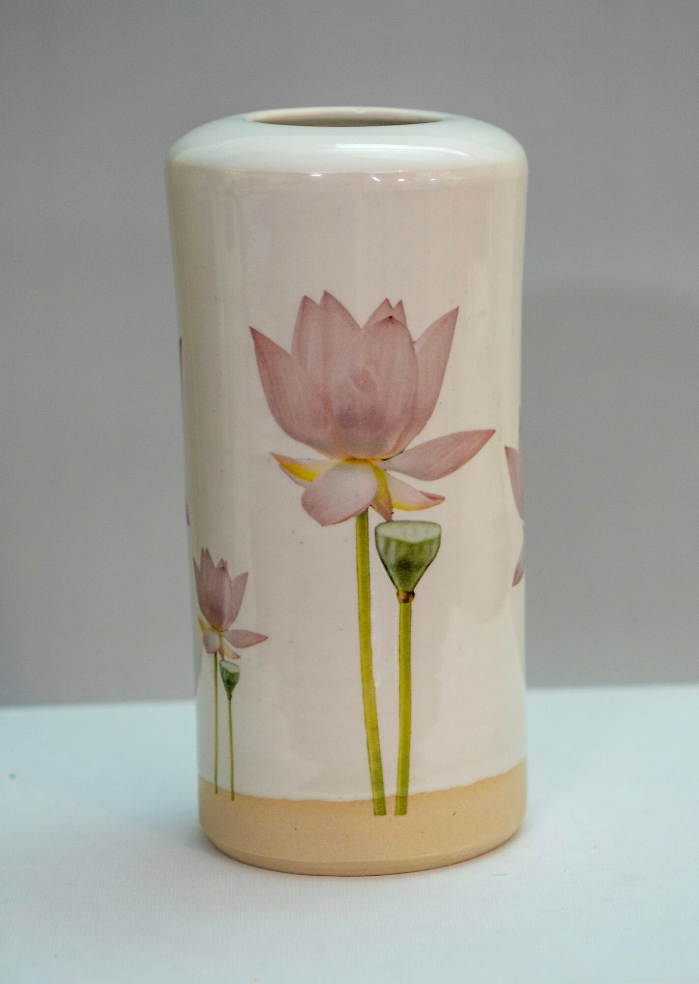 Ceramic vase with pink lotus flower design, cylindrical shape, cream background, and a beige base.