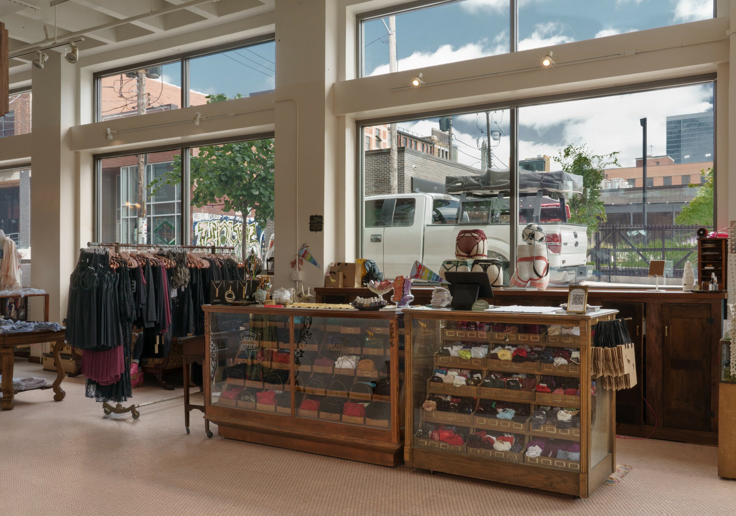 Clothing store interior with racks of clothes, display cases, and large windows showing street view.