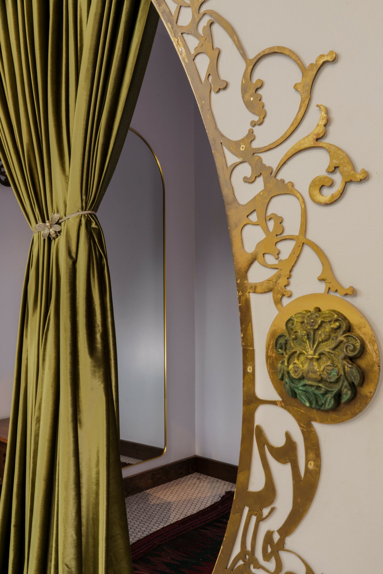Decorative gold ornate wall with a circular element and a green and gold floral design, next to a green curtain.