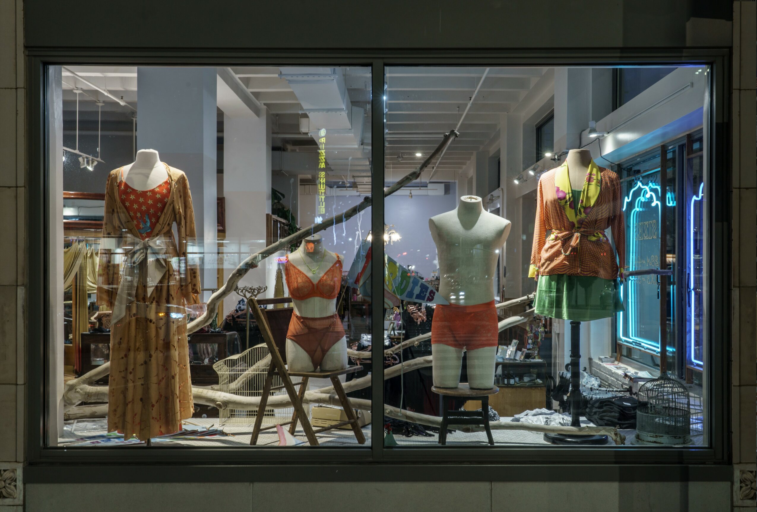 Store window display with mannequins dressed in colorful clothing, inside a shopping mall.