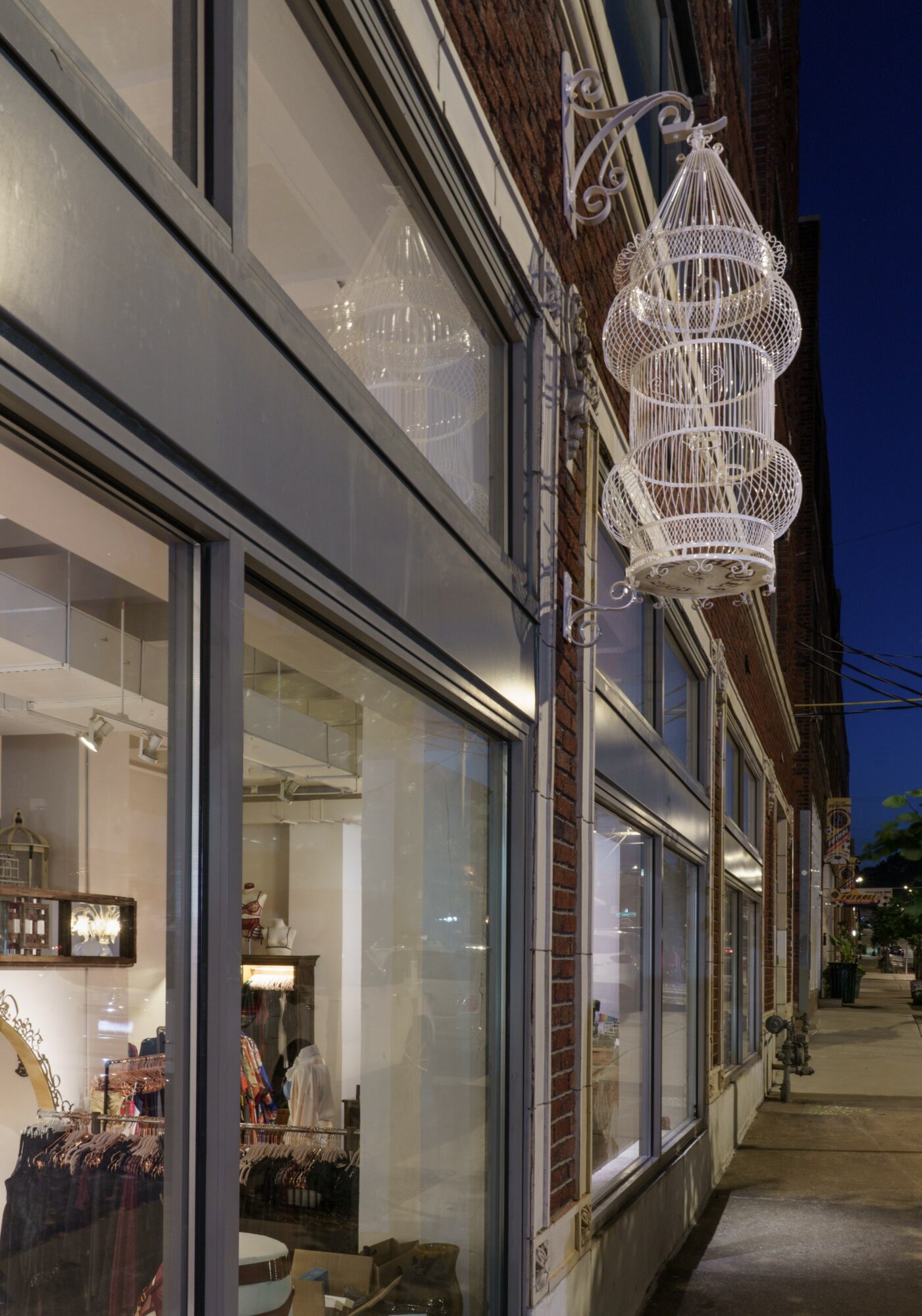 Nighttime street view with large windows and a hanging decorative light fixture outside, sidewalk visible, building facade with brick and glass.