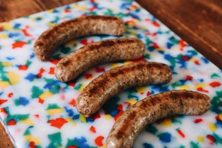 Five cooked sausages on a colorful, patterned plate with red, blue, yellow, and green shapes, on a wooden surface.
