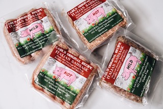 Four packages of small Italian sausage with pink pig illustrations and red, green, and white labels, on a white surface.