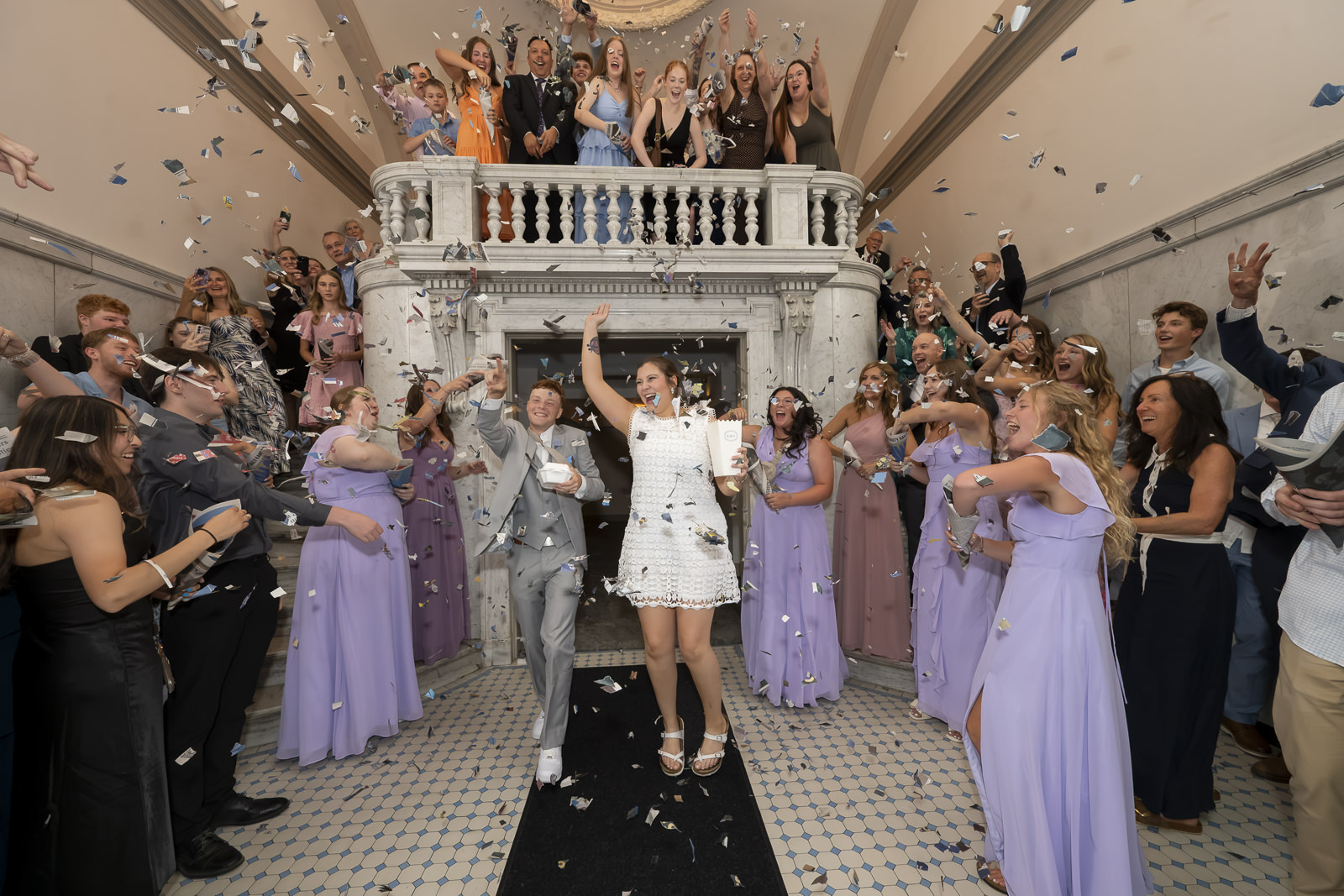 People celebrating at a wedding reception with a bride and groom dancing, surrounded by guests in formal attire, confetti falling.