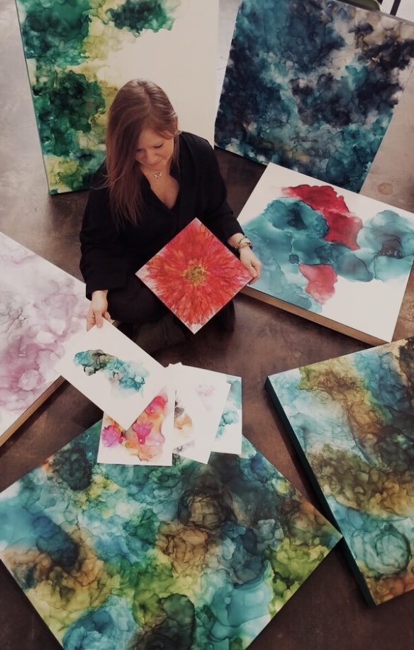 Person holding a red and yellow abstract painting surrounded by other colorful abstract artworks on the floor.