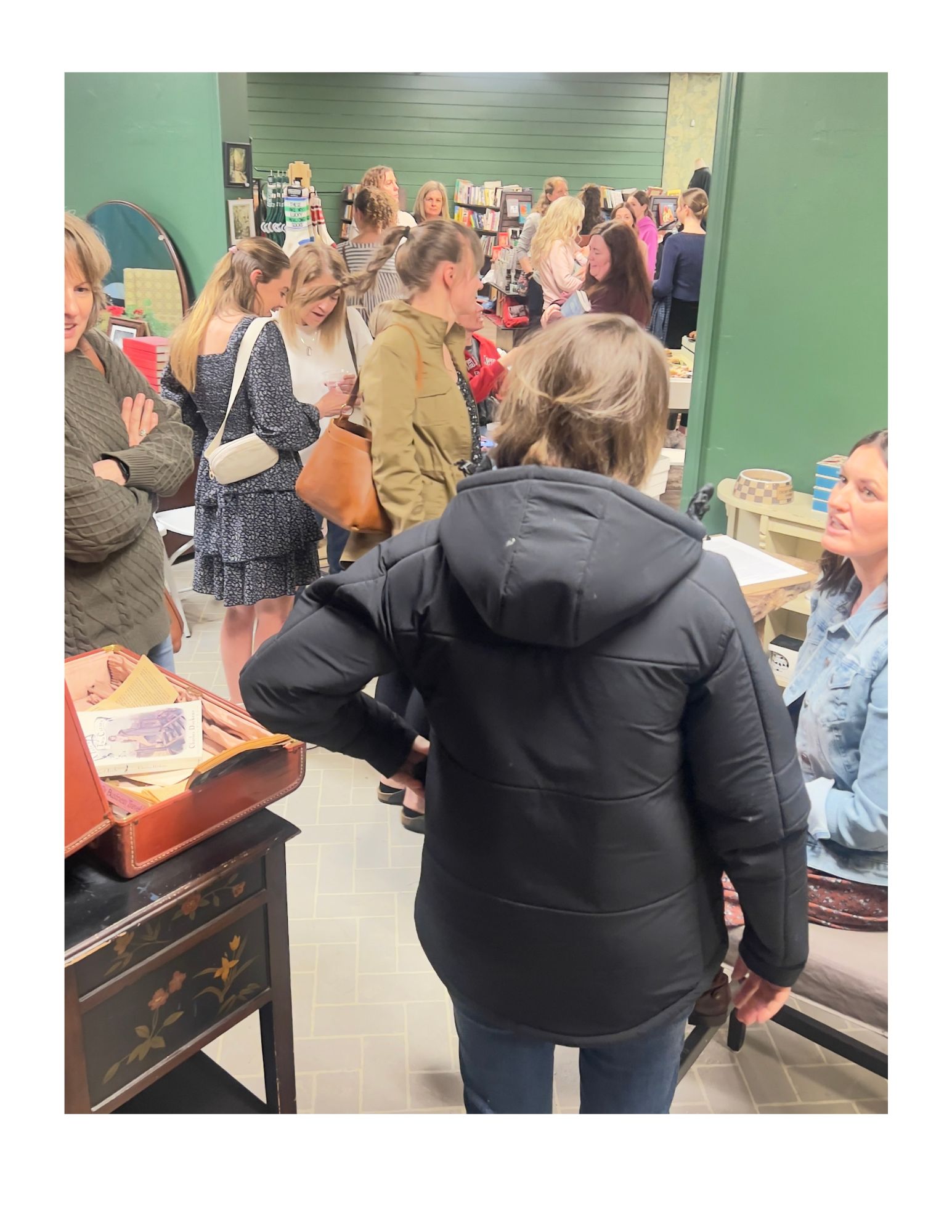 People gathered around a table in a store or market, engaging in conversation and browsing items.