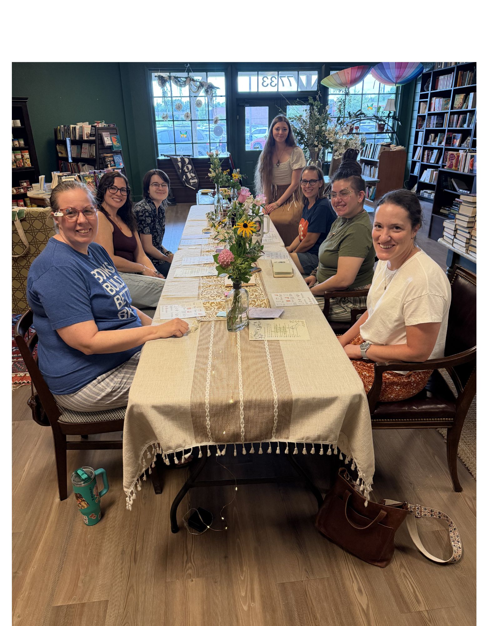Group of seven people sitting around a table in a room with bookshelves and large windows, some smiling at the camera.