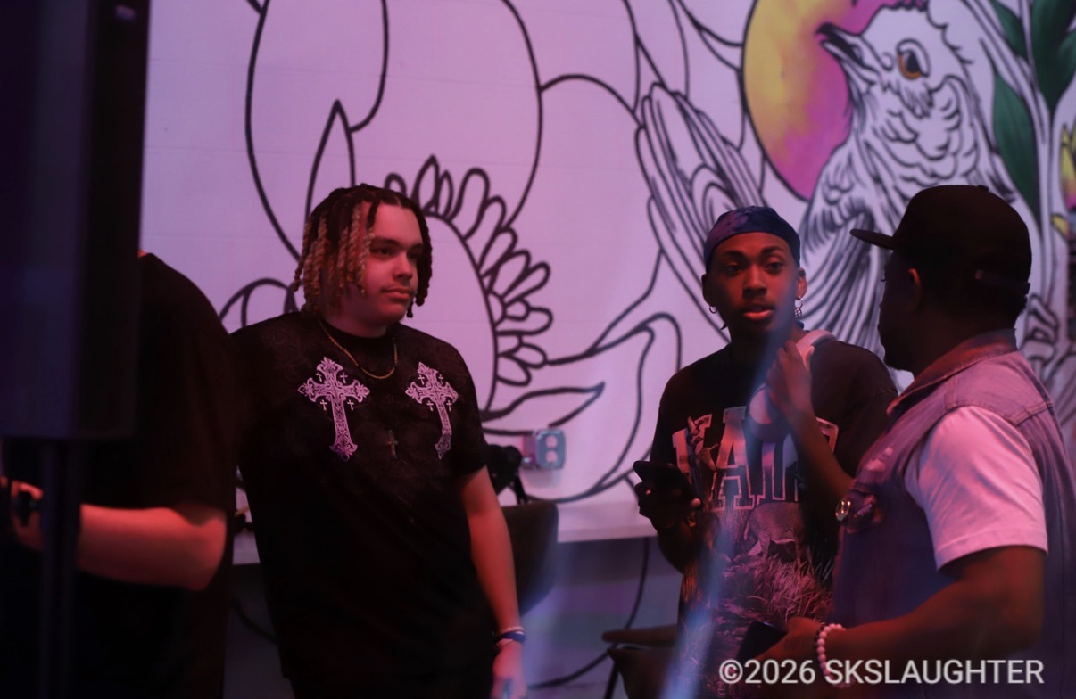 Three people standing in front of a colorful mural with animals and plants, engaging in conversation.