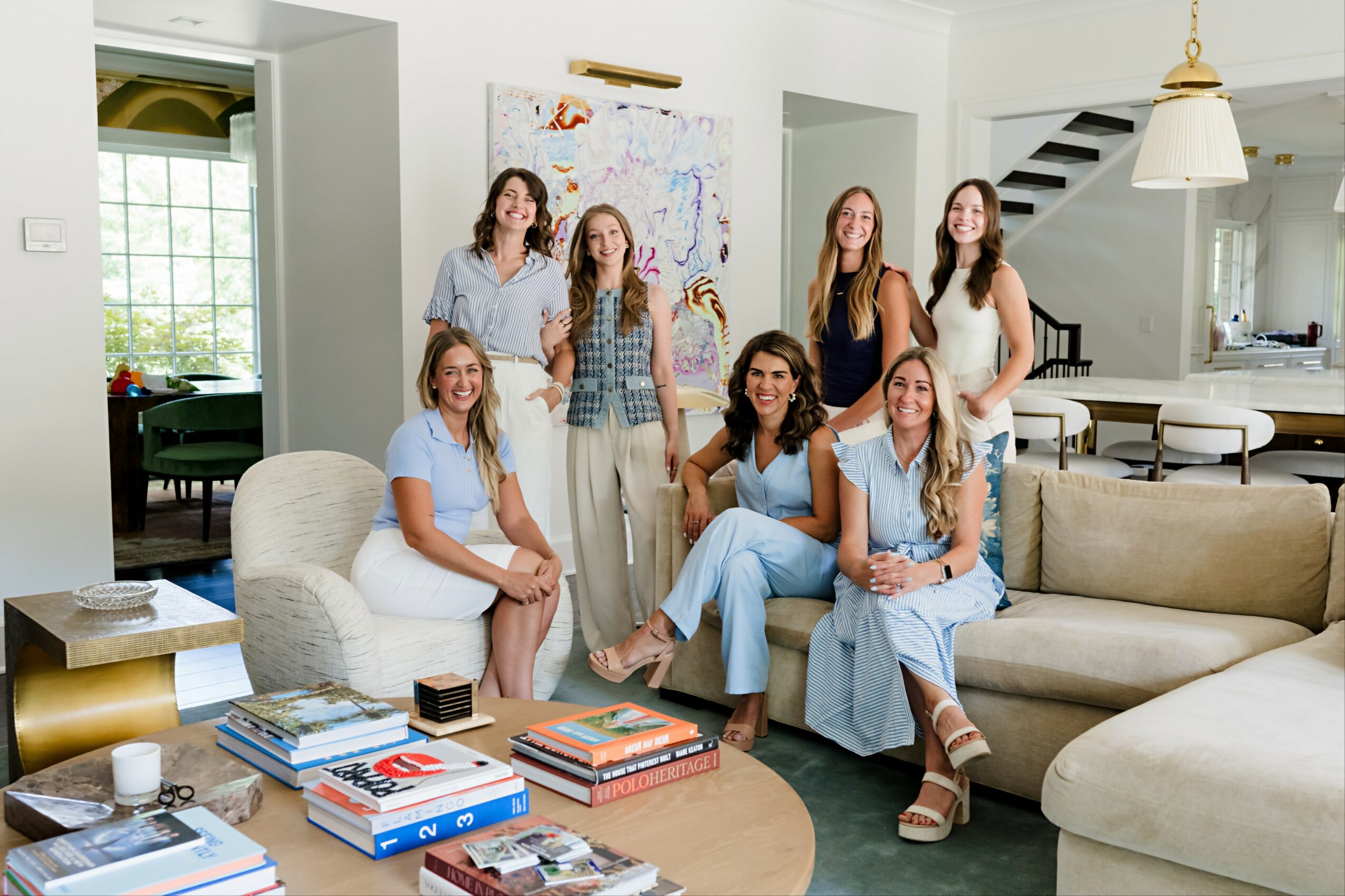 Group of seven women sitting and standing in a living room with books and a map on the wall.