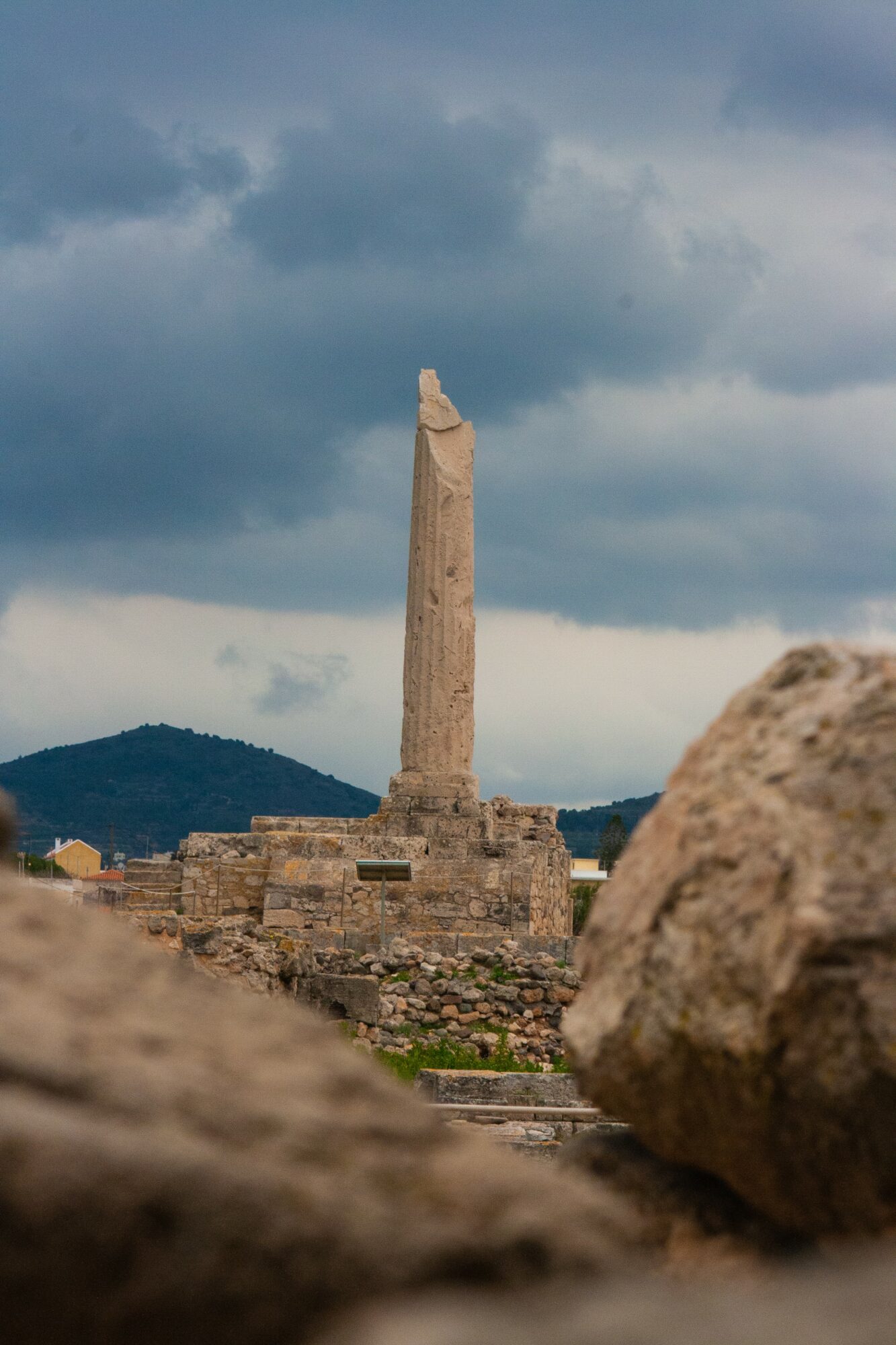 Ancient stone monument against cloudy sky, with rocks in foreground and distant hills, in a historical site.