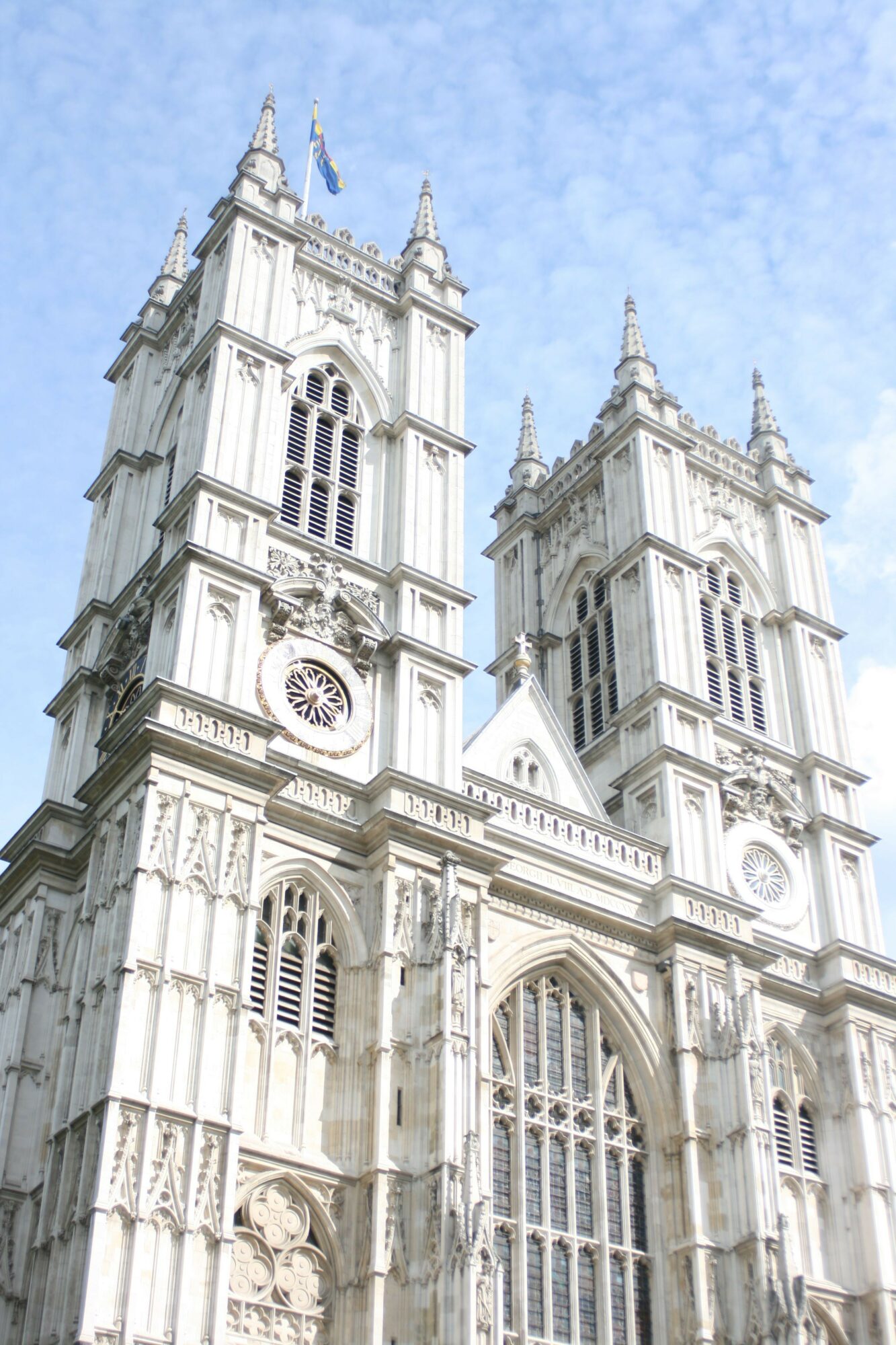 A historic white building with ornate architectural details and a clock, set against a blue sky with clouds.