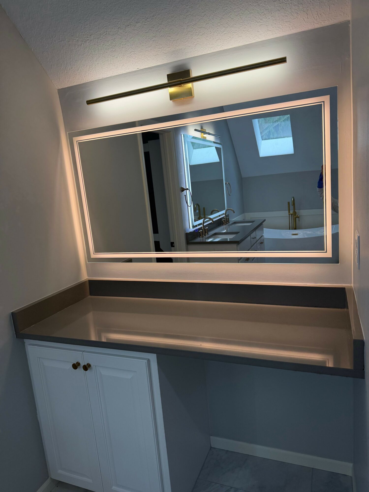 Mirror reflecting a room with a window and ceiling light, with a wall-mounted light fixture nearby.