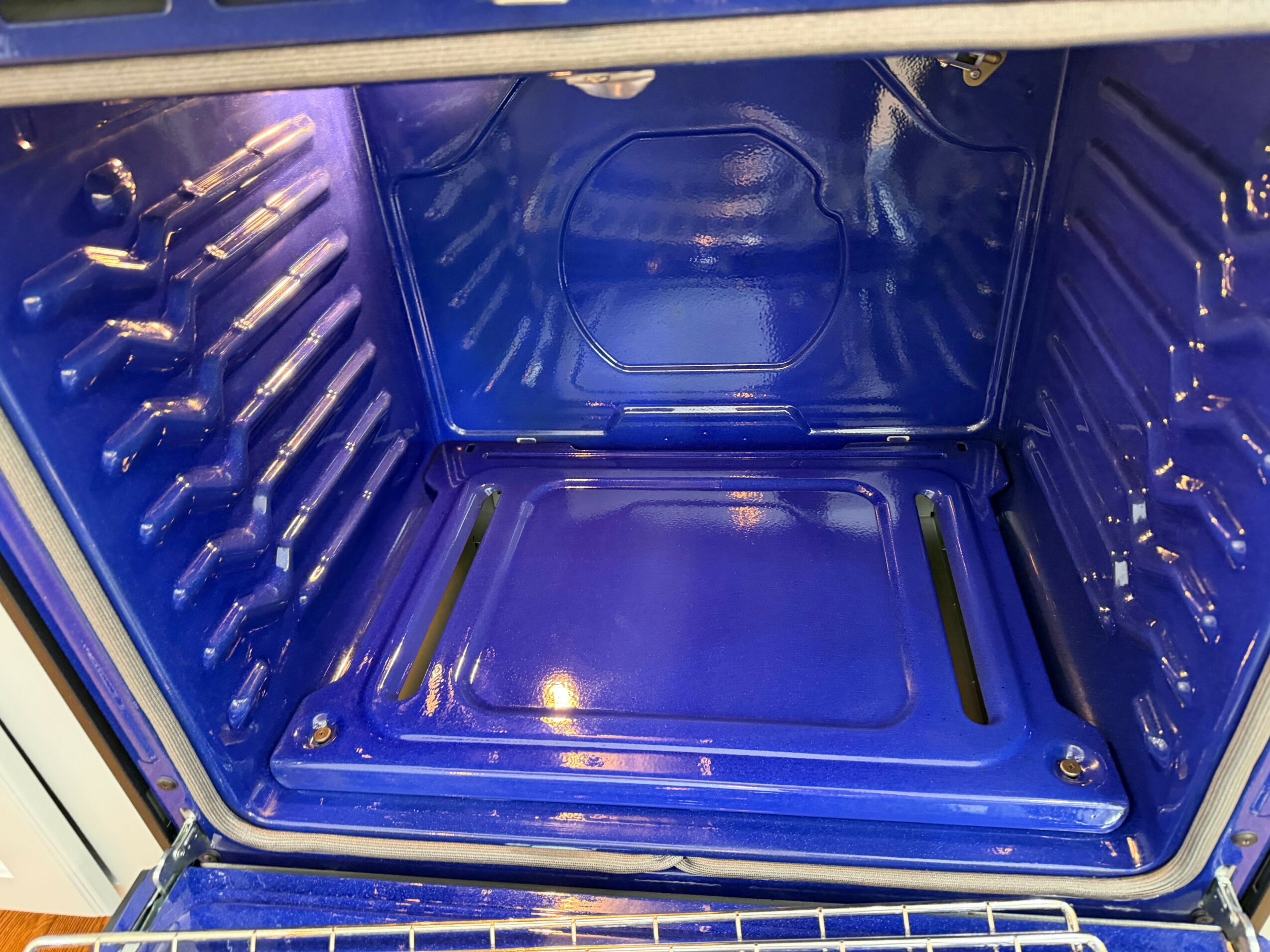 Inside of a blue oven with metal racks and a shiny interior, viewed from the front.