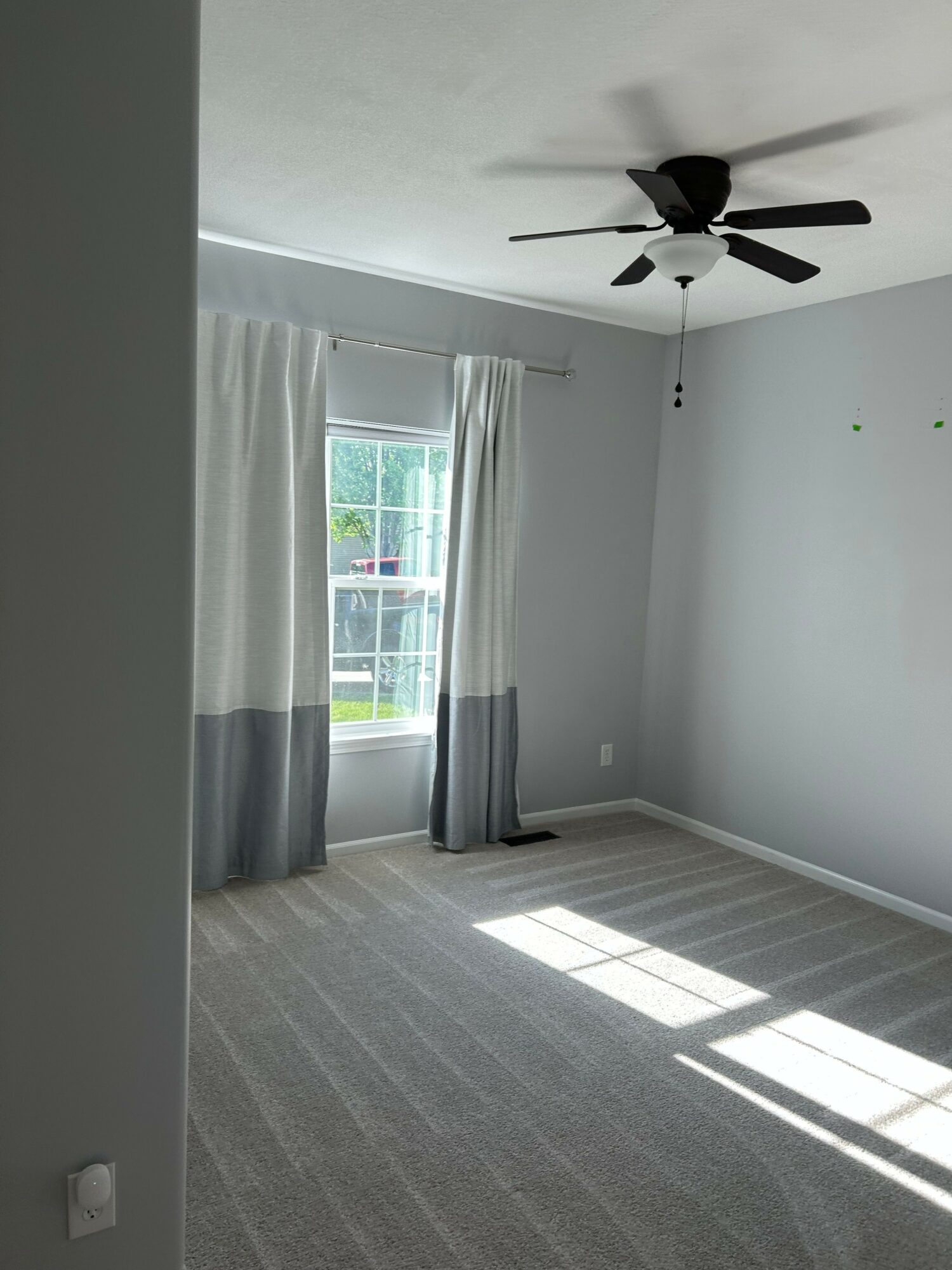 Empty room with window, curtains, ceiling fan, and sunlight on the floor.