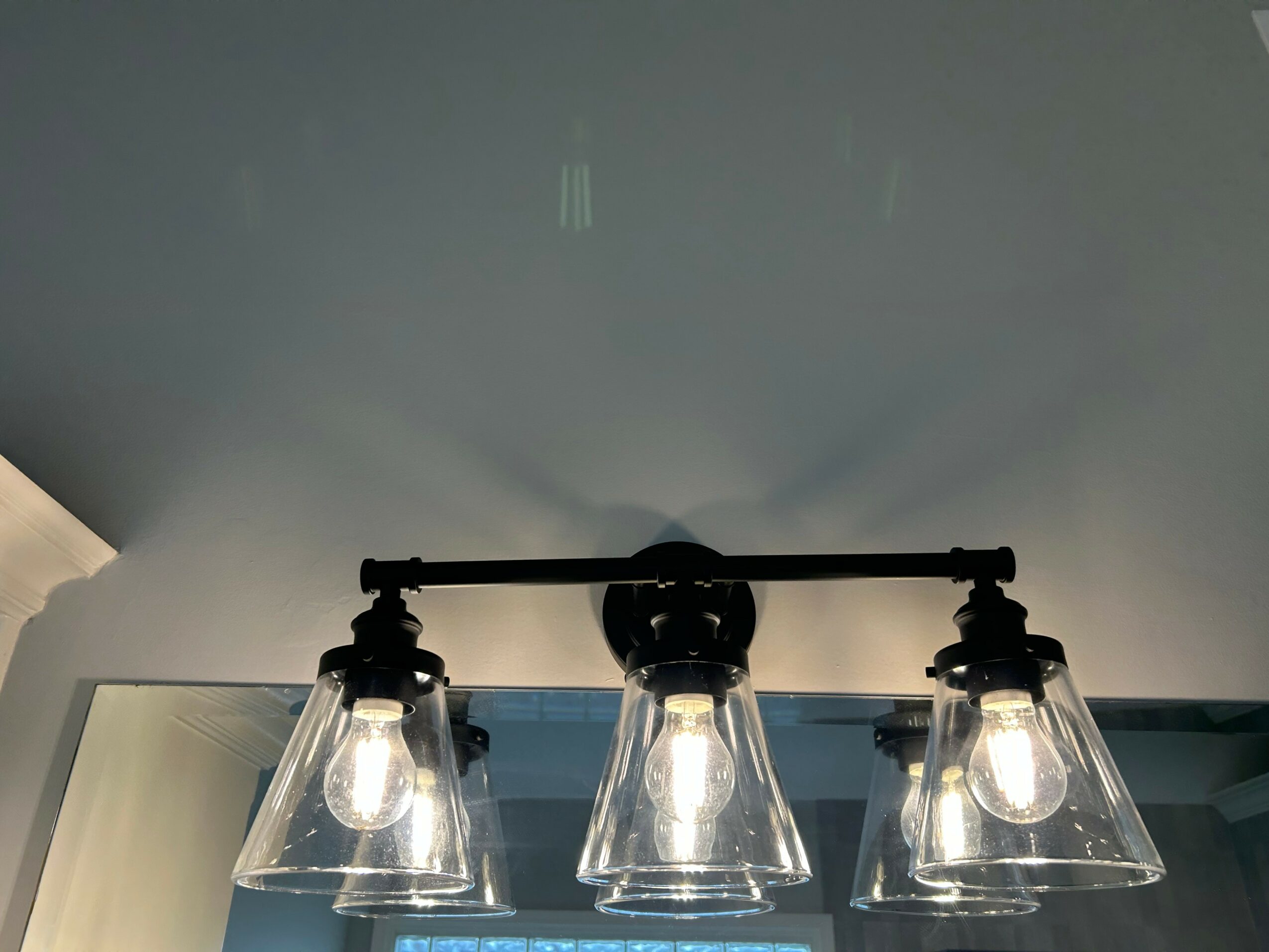 Ceiling light fixture with three glass shades and exposed bulbs, mounted on a ceiling with a shadow cast below.