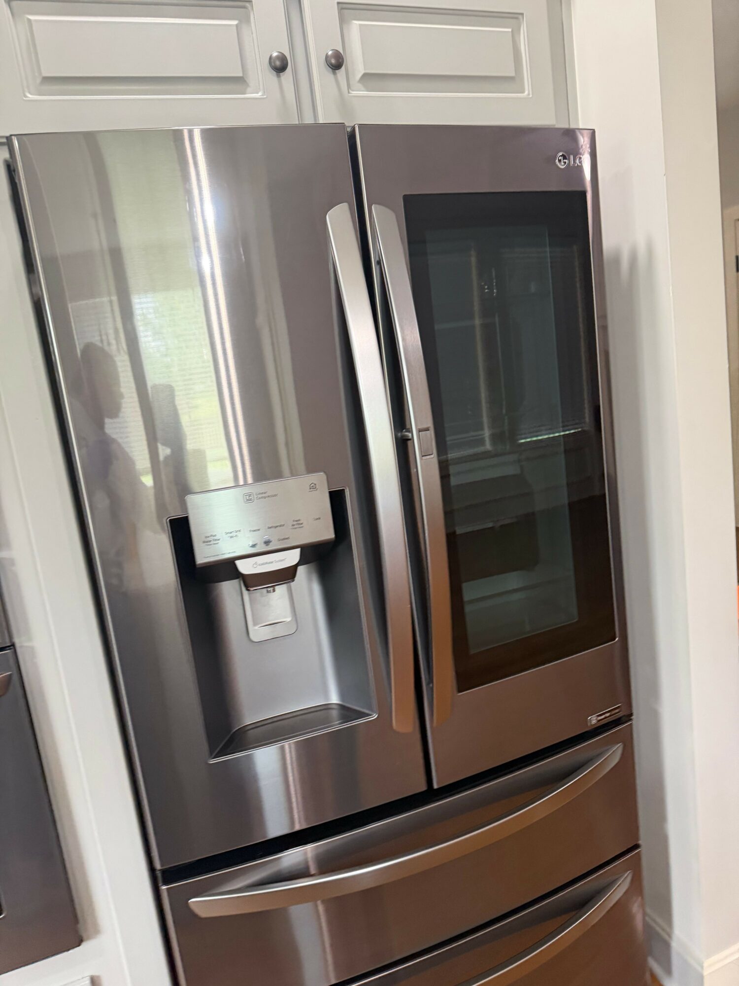 Stainless steel refrigerator with a water and ice dispenser, installed in a kitchen with white cabinetry.