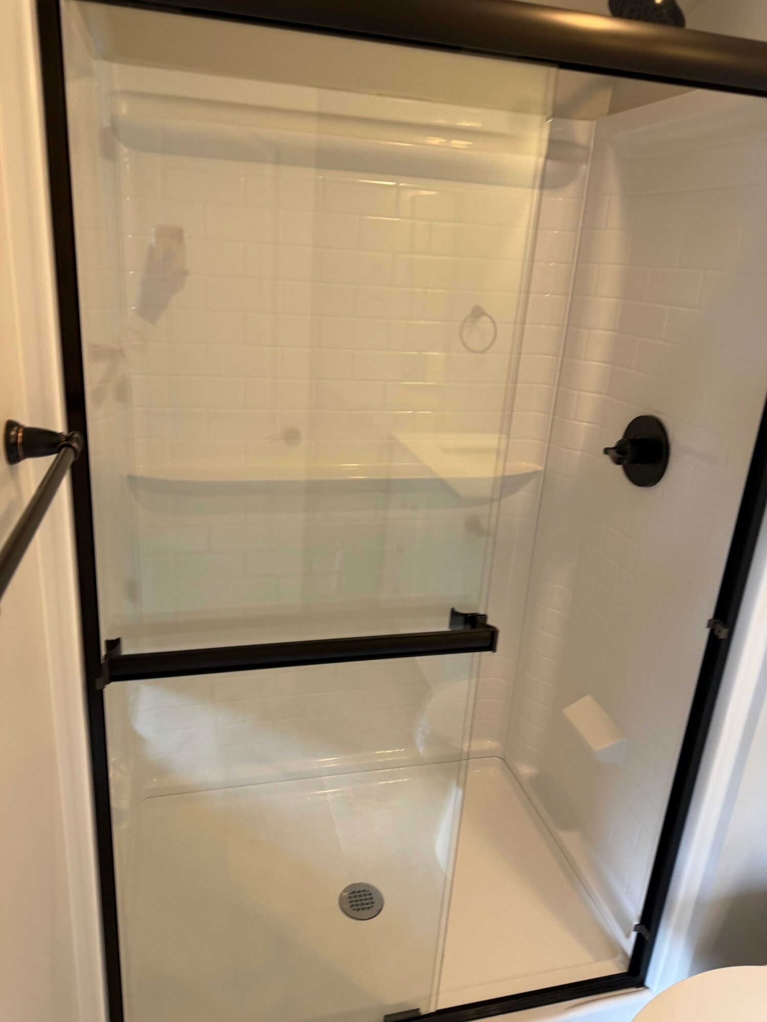 View of a shower with a glass door, white tiled walls, and a ceiling light fixture.