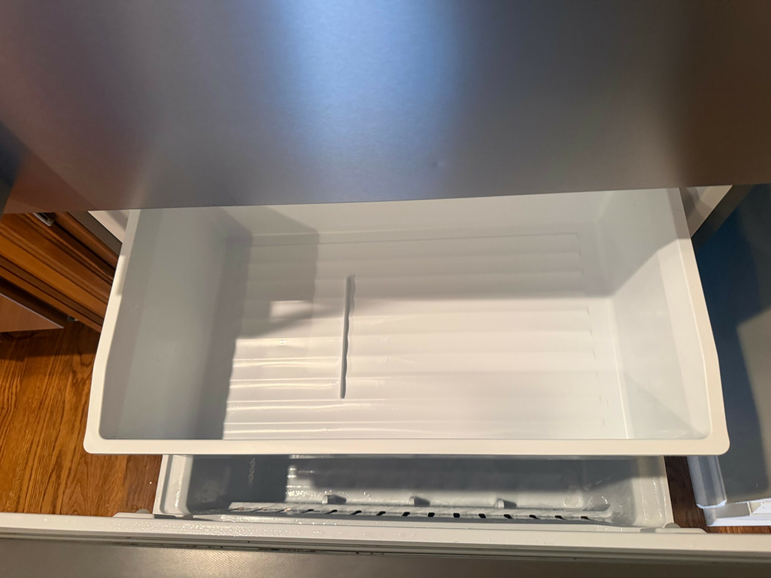 Open empty drawer with white interior, partially pulled out from furniture, with a shadow on the back wall.