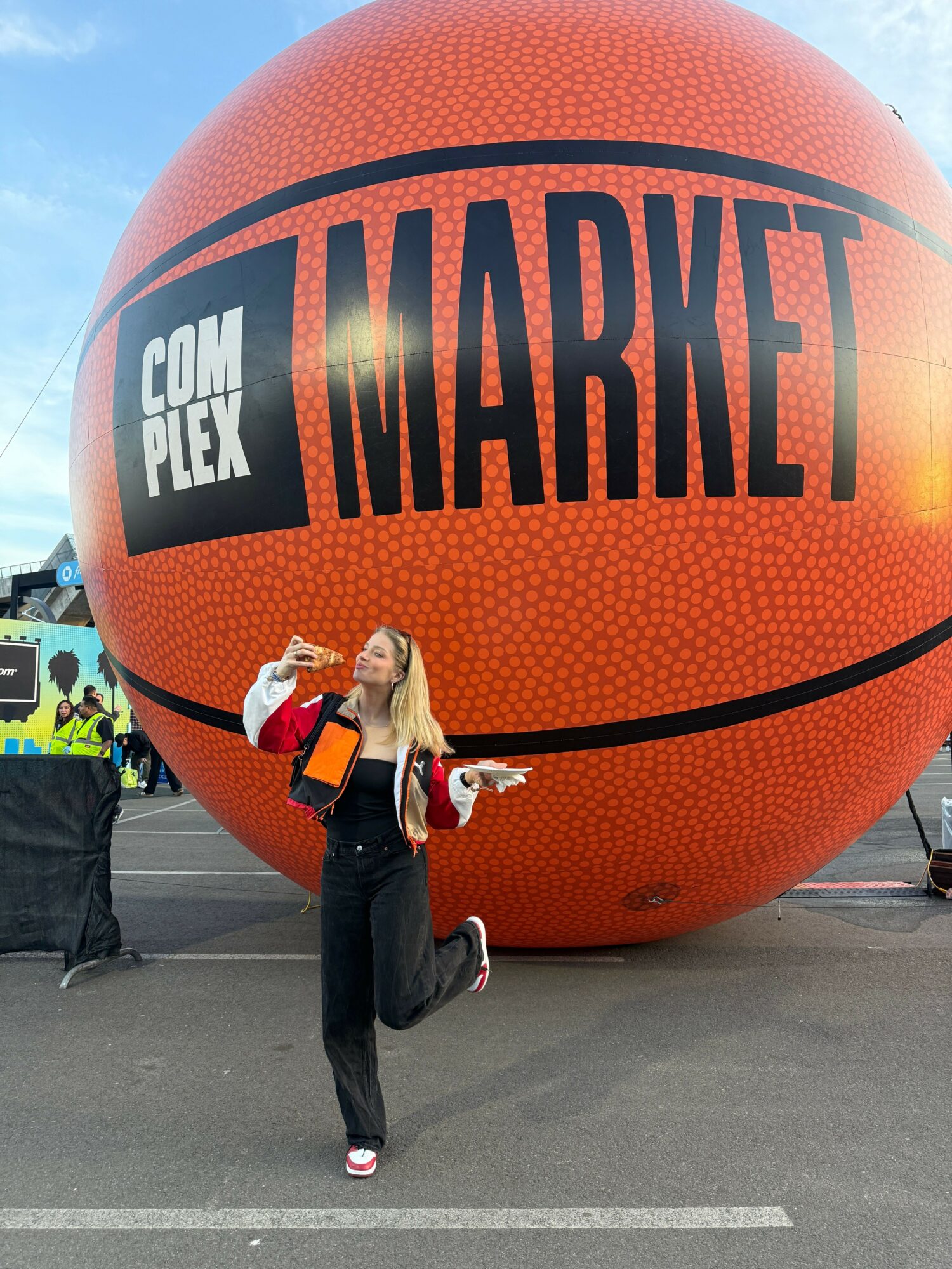 Person standing next to a large orange basketball-shaped structure with 'COMIX PLEX' and 'MARVEL' written on it, holding a phone.
