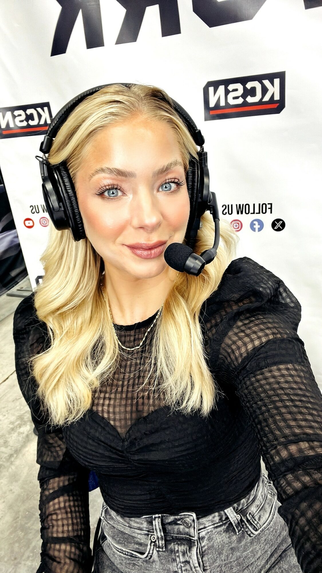 Young woman with blonde hair wearing a headset and black mesh top, smiling in front of a KSN backdrop.