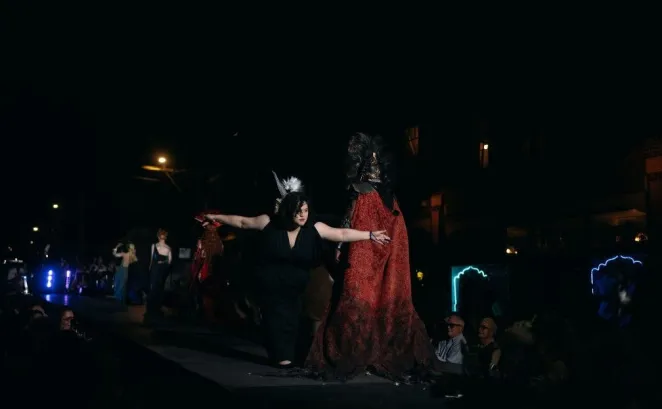 Two women dance on stage at night, with a dark background and some illuminated people and decorations.